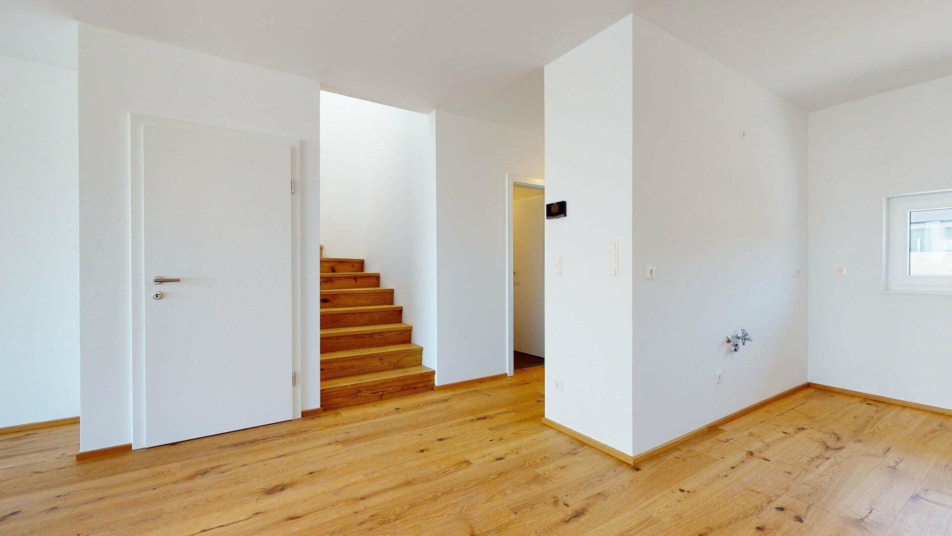 Heller Eingangsbereich mit Holztreppe und Parkettboden, führt zu den oberen Etagen.