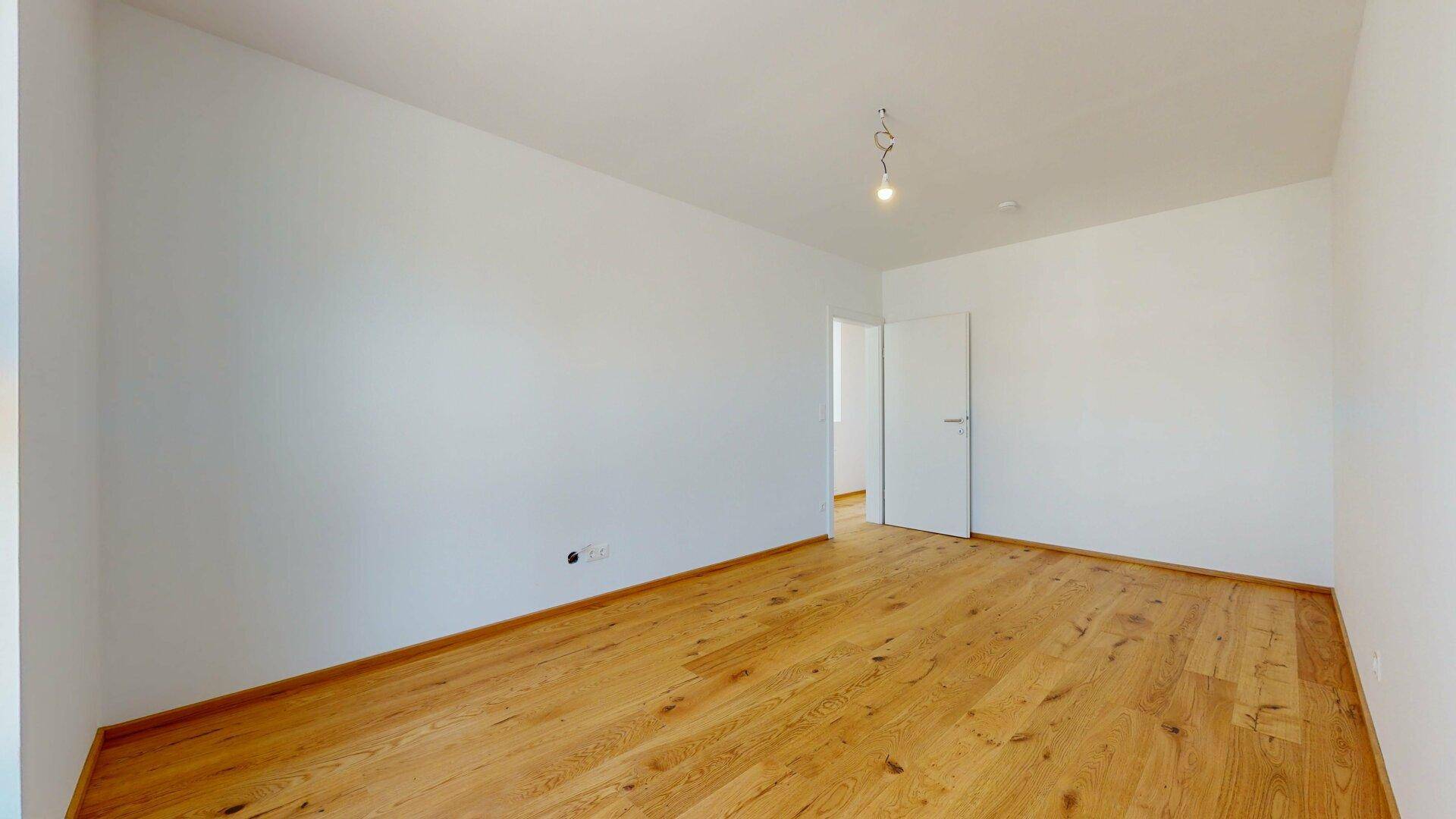 Leeres Zimmer mit Holzboden und weiß gestrichenen Wänden, bereit zum Einzug.