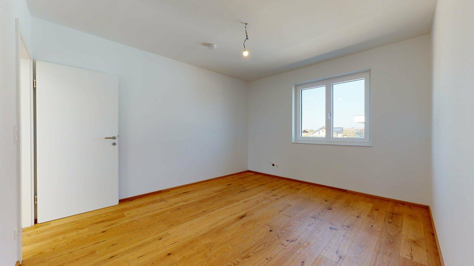 Leerer Raum mit hellem Holzboden und Fenster, bietet viel Tageslicht und eine neutrale Basis.