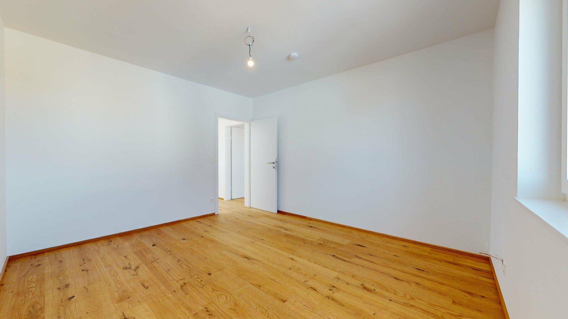 Leeres Zimmer mit Holzboden und weiß gestrichenen Wänden, bereit für neue Bewohner.
