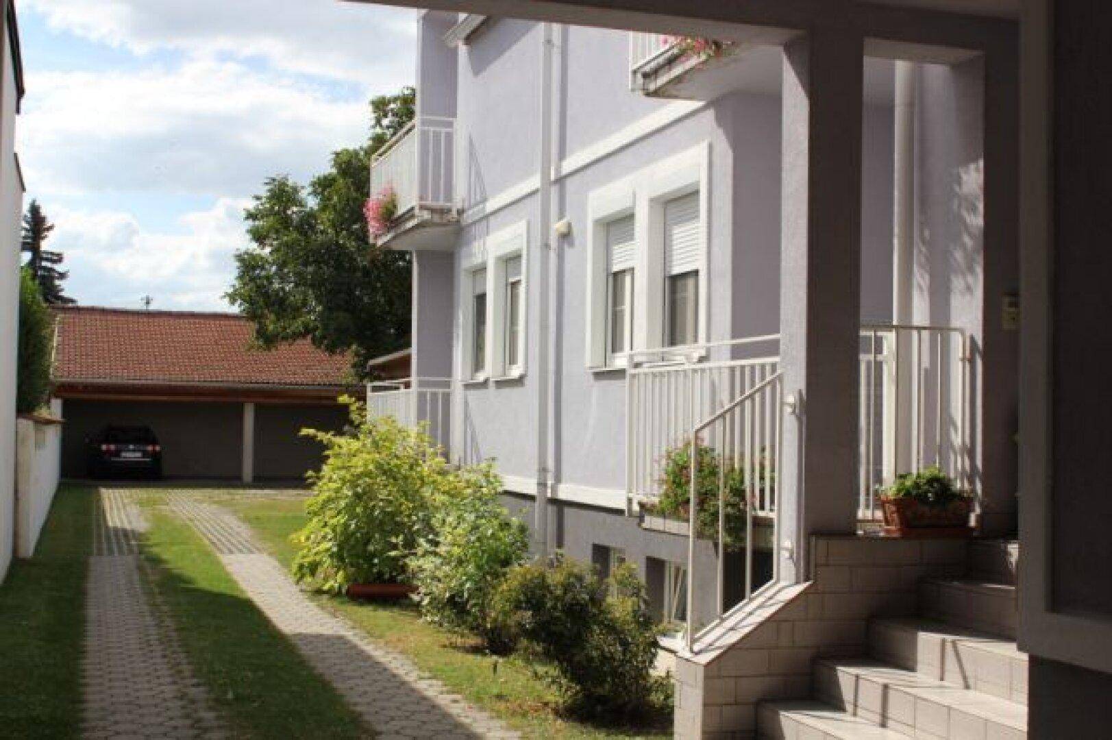 Seitenansicht des Gebäudes mit Eingangsbereich, Balkonen und Zufahrt zum Carport im Hintergrund.