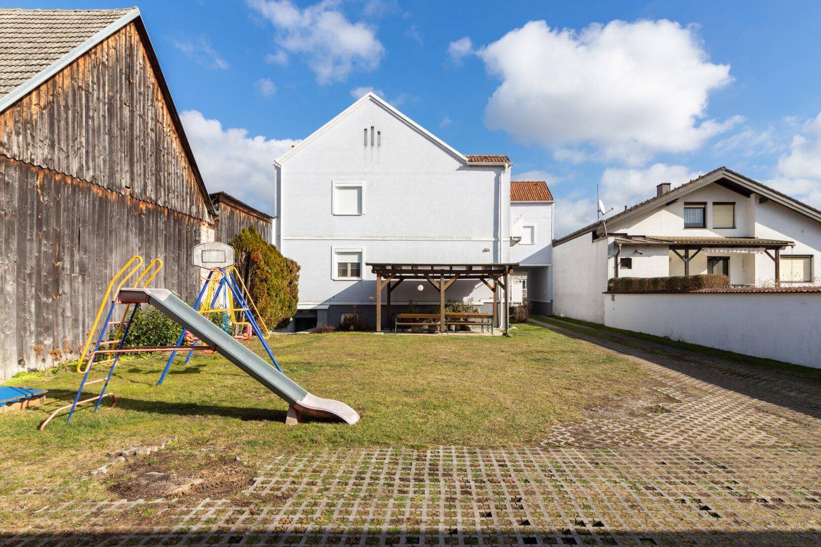 Weitläufiger Garten mit Kinderrutsche, Schaukel und überdachtem Essbereich im Freien.