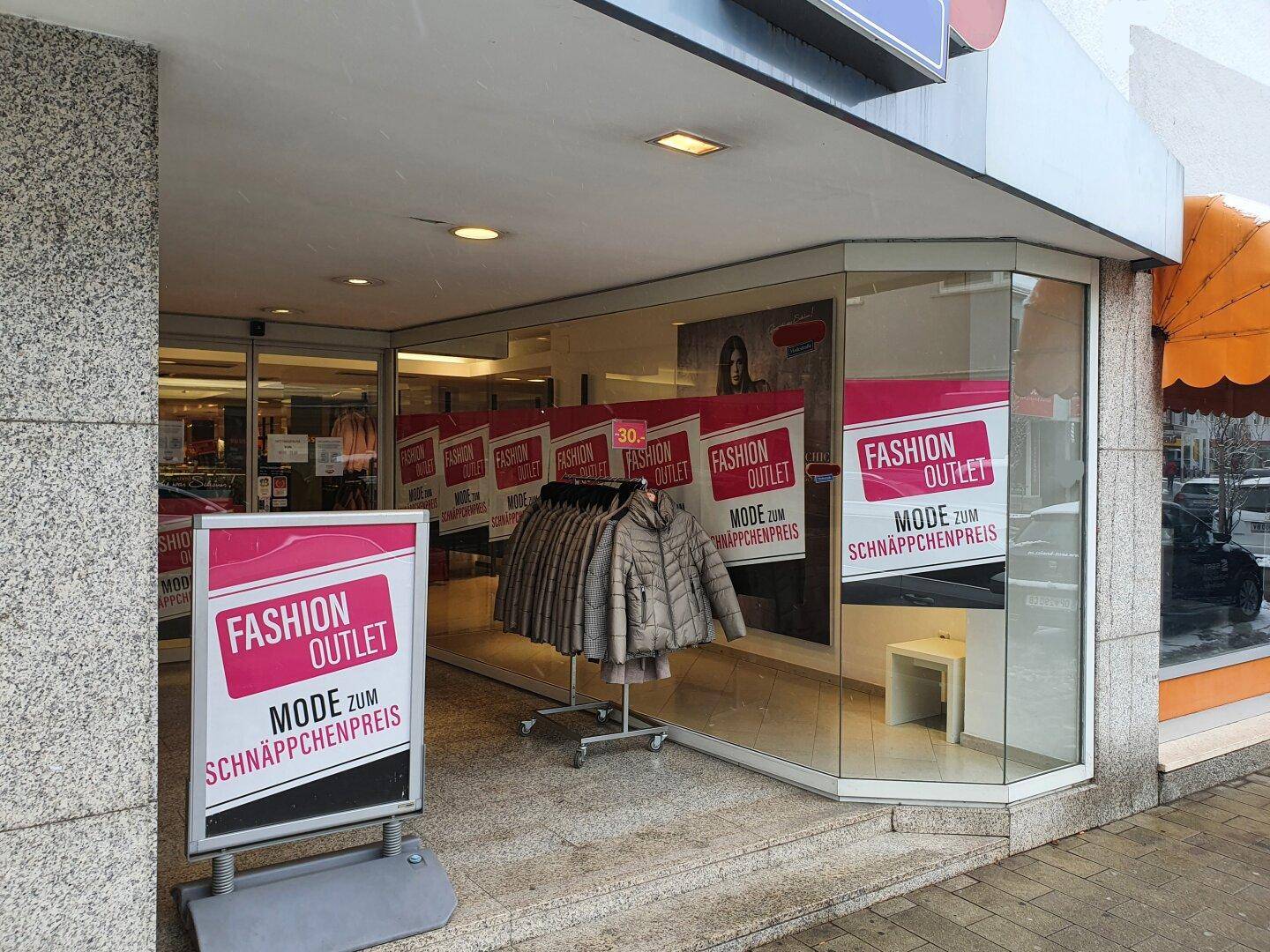 Außenansicht eines Geschäfts mit großen Schaufenstern und Werbeplakaten.