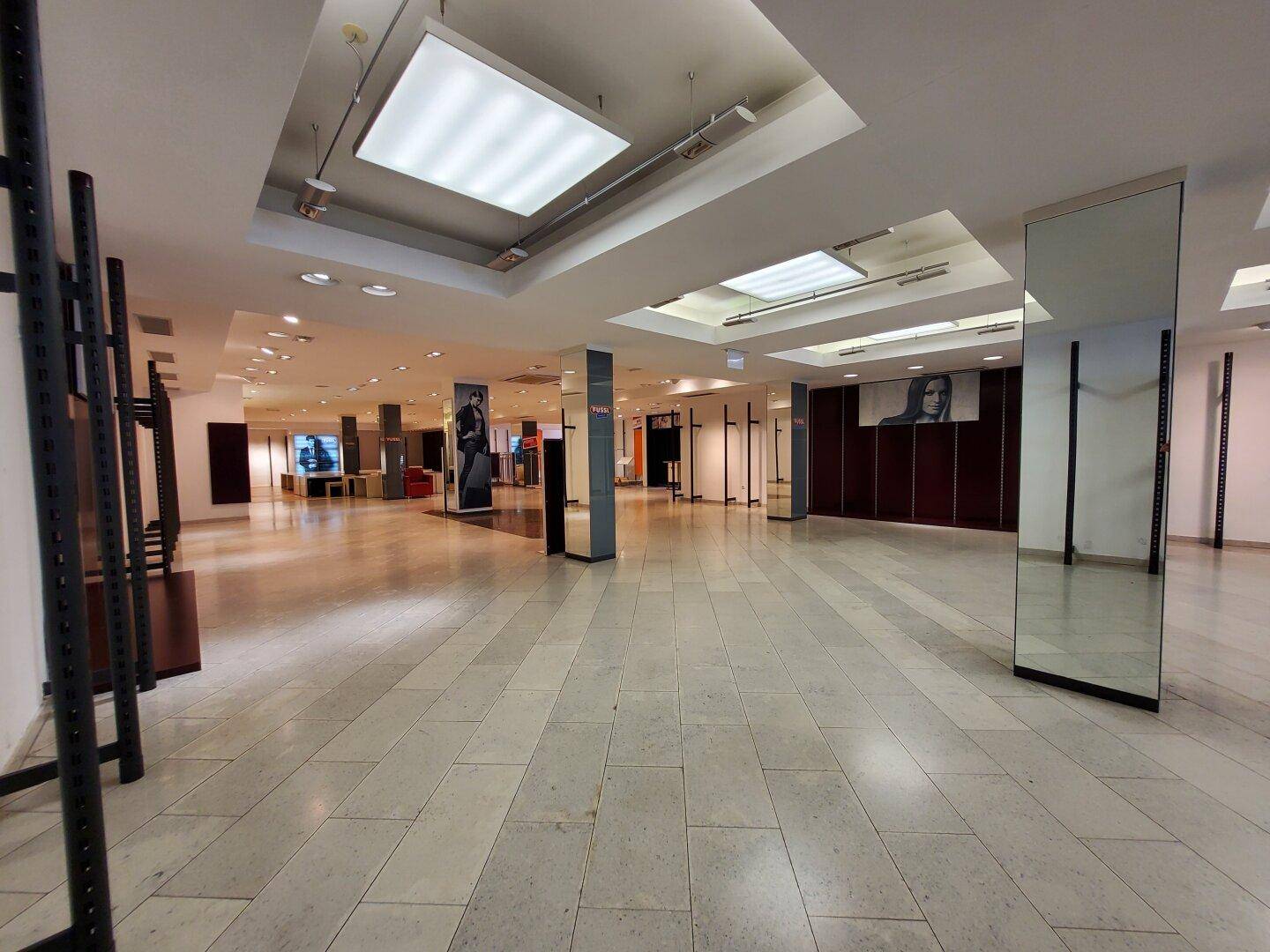 Großer, leerer Verkaufsraum mit Fliesenboden und spiegelnden Säulen.