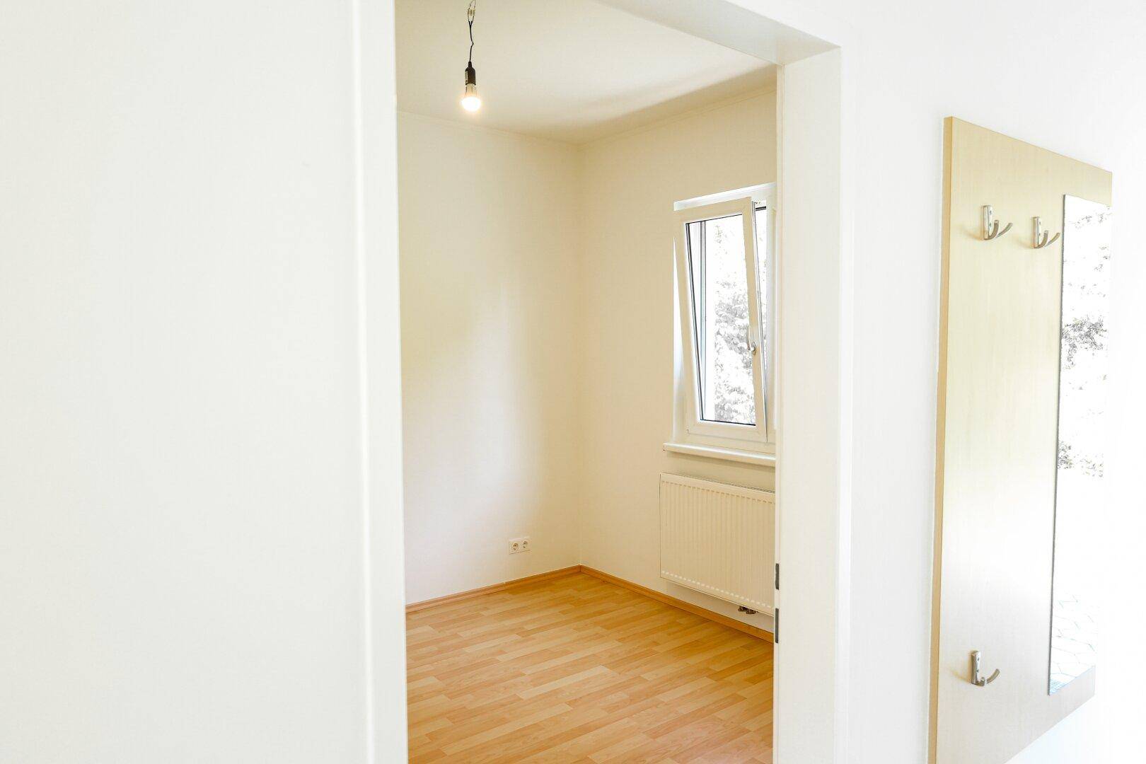 Heller Raum mit Laminatboden und Fenster, gesehen durch einen Türrahmen.