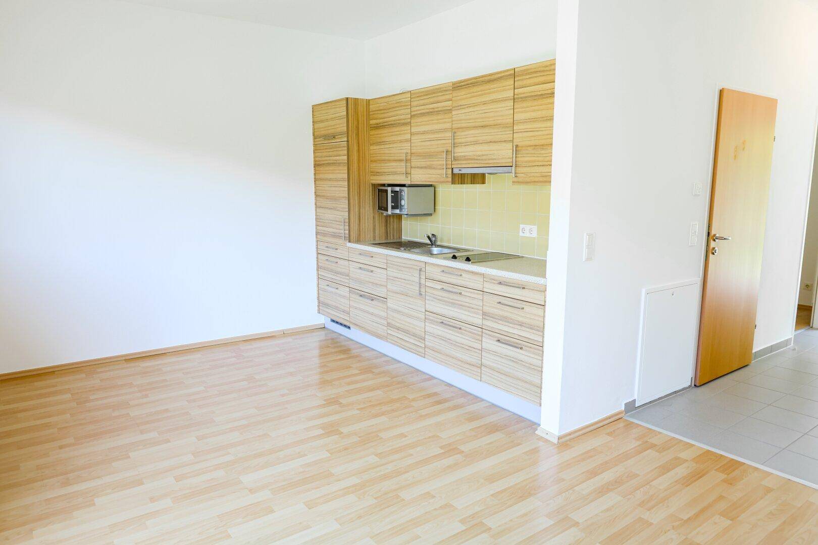 Moderne Küchenzeile mit Holzfronten und integrierter Mikrowelle in hellem Raum.