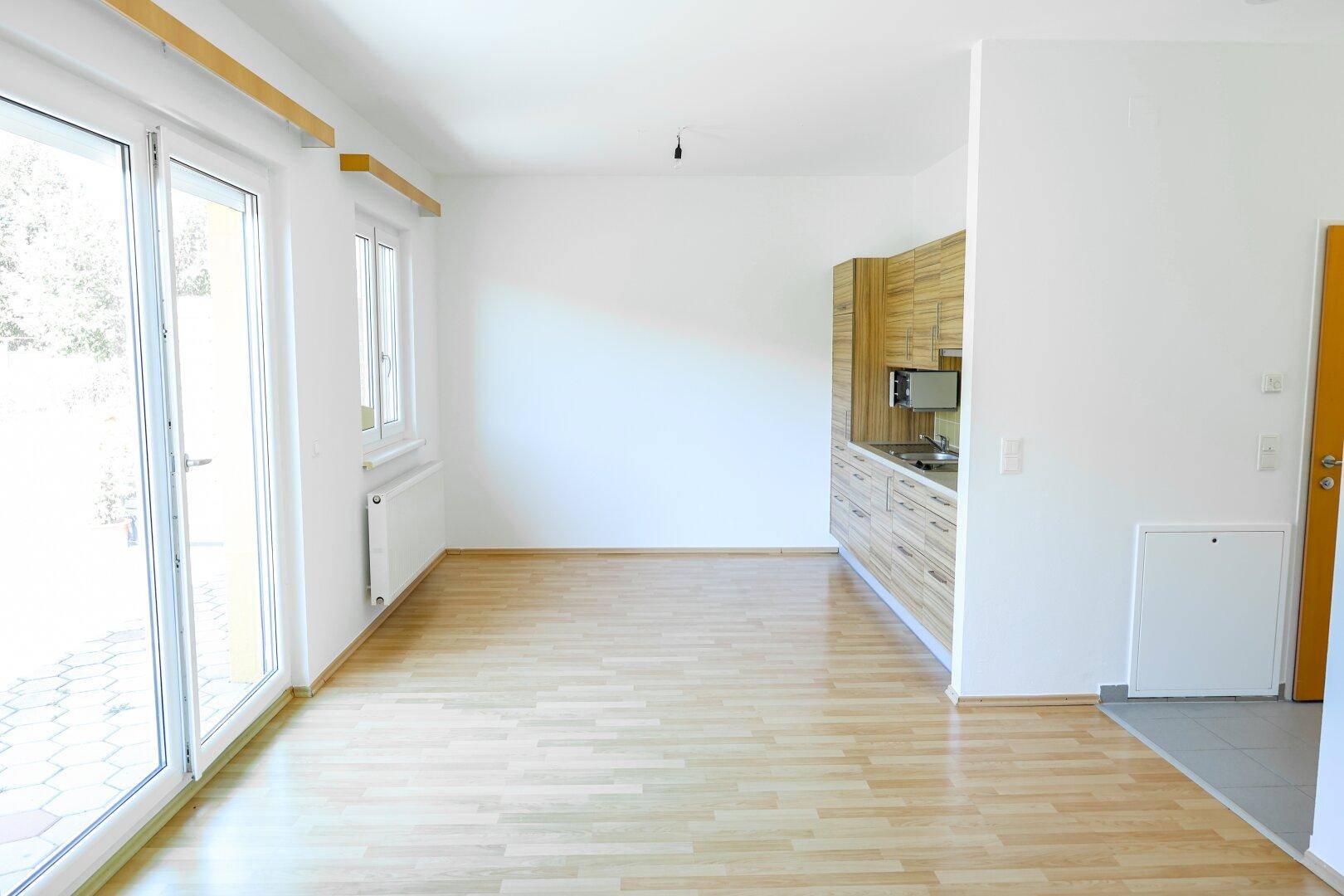 Geräumiger, heller Raum mit Laminatboden, Küchenzeile und Zugang zur Terrasse.