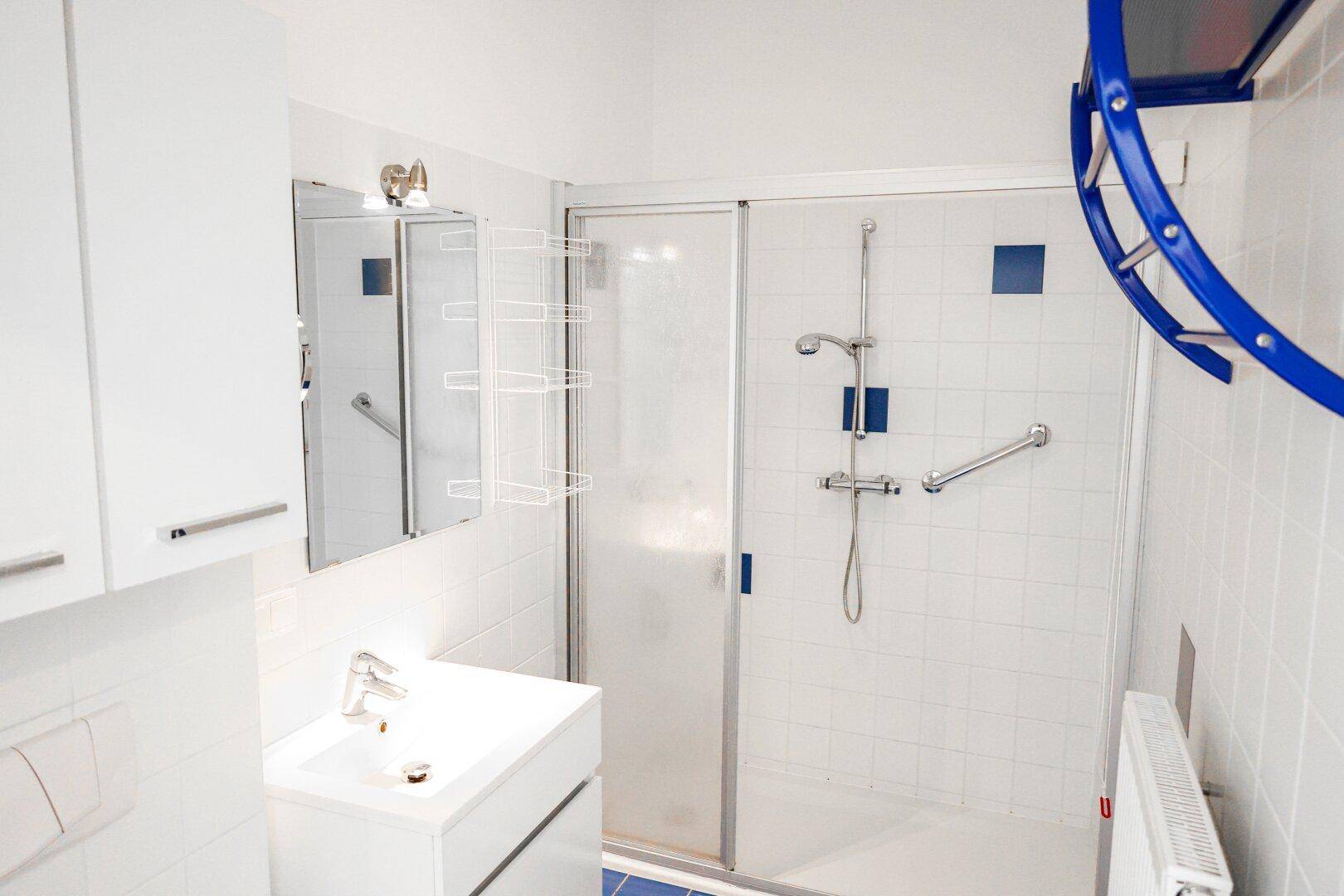 Modernes Badezimmer mit ebenerdiger Dusche, blauen Fliesen und Haltegriffen.