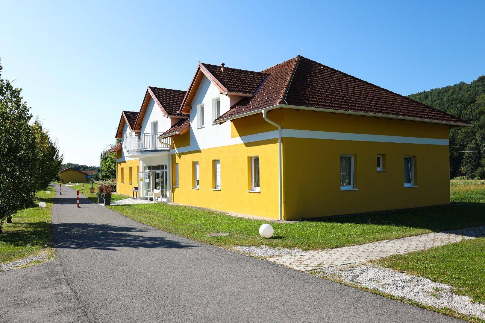 Größeres gelb-weißes Gebäude mit Zufahrt und gepflegter Grünfläche.