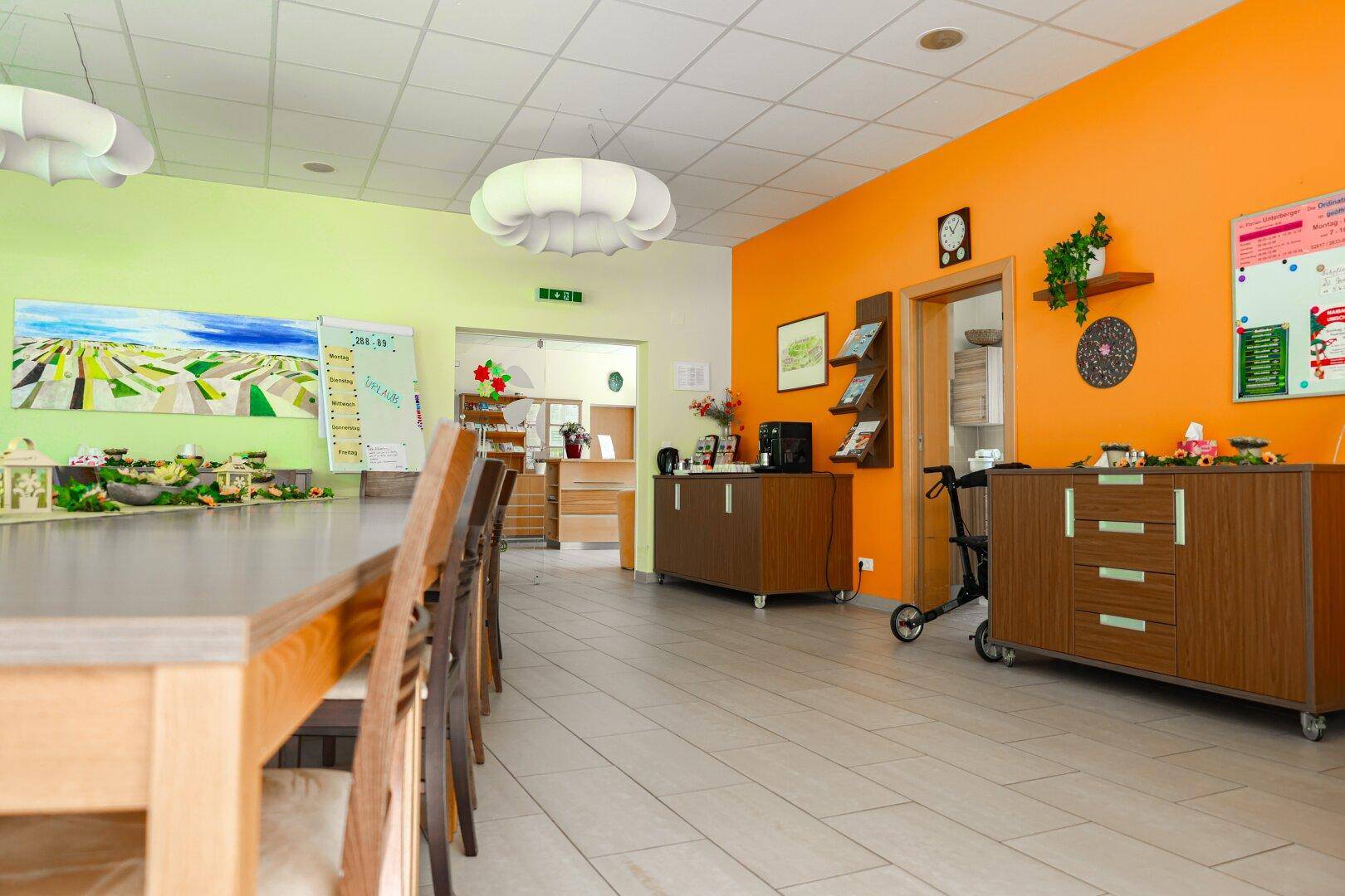 Großer Gemeinschaftsraum mit langen Tischen, bunten Wänden und Fliesenboden.