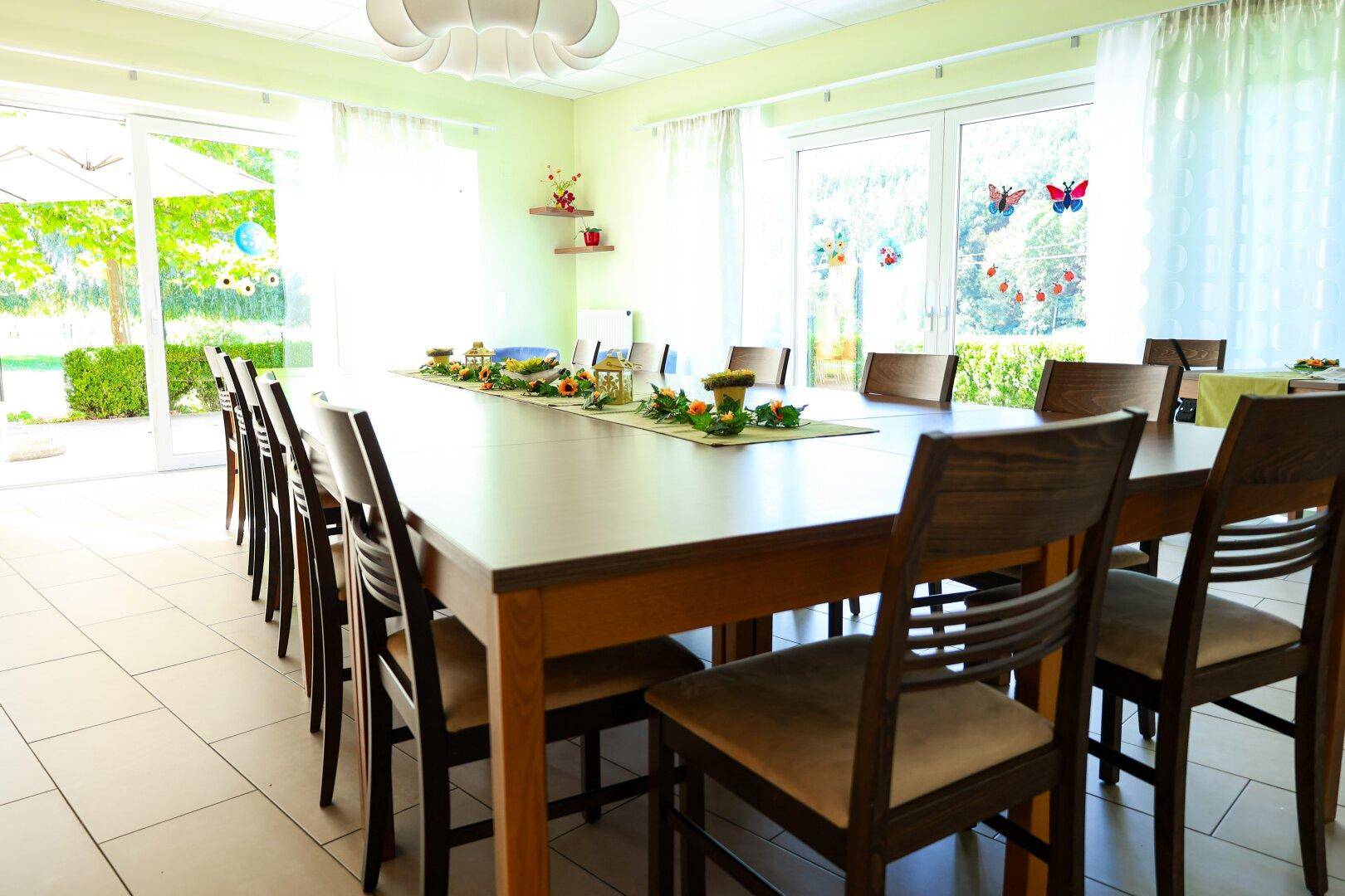 Heller Gemeinschaftsraum mit langen Tischen und großen Fenstern mit Blick ins Grüne.