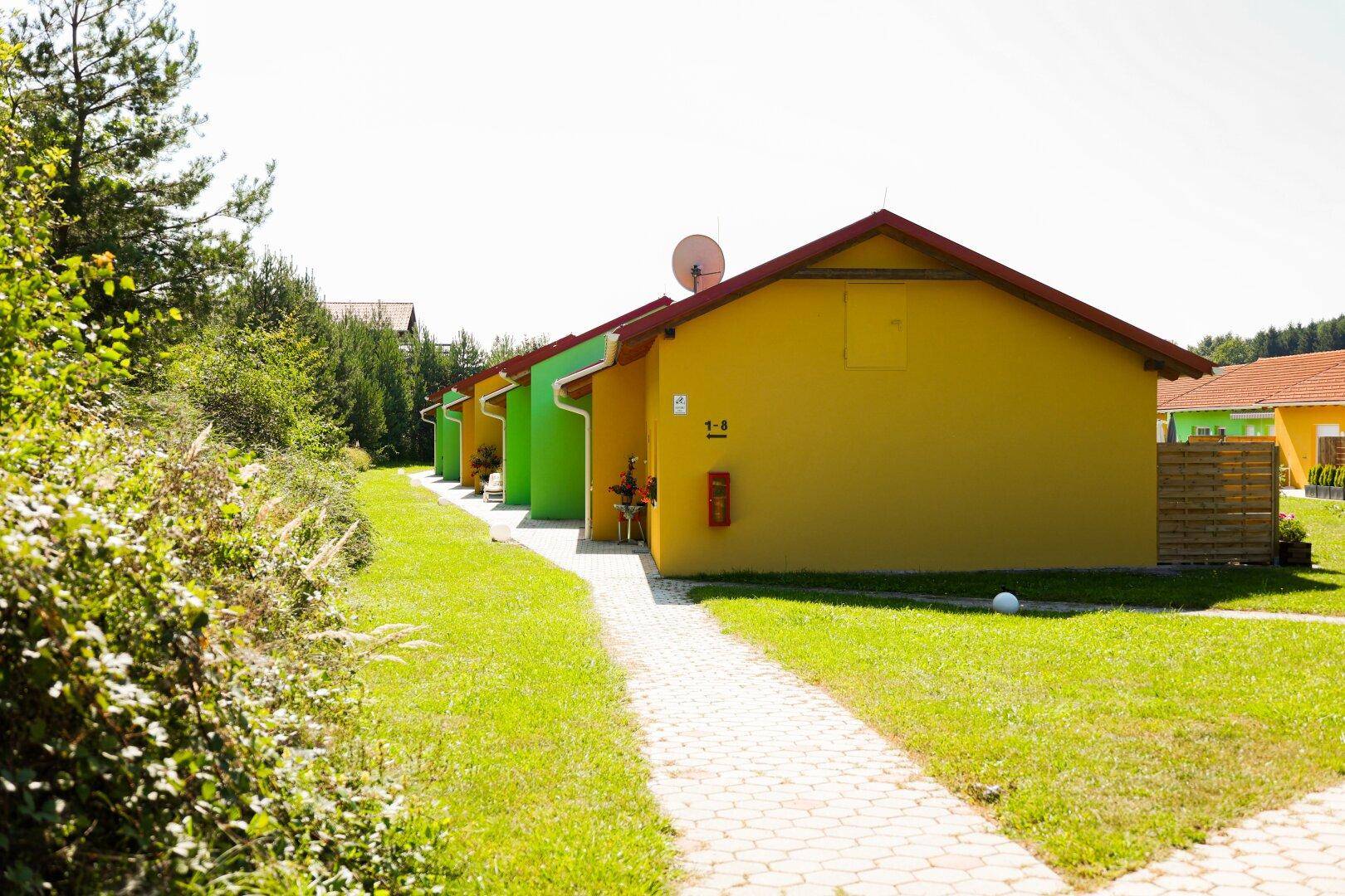 Reihe bunter Häuser entlang eines gepflasterten Weges, umgeben von üppigem Grün.