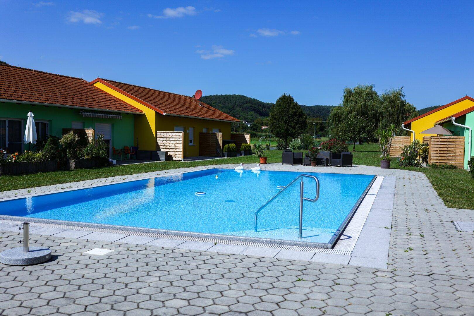 Außenpoolbereich mit Liegemöglichkeiten und bunten Häusern im Hintergrund.