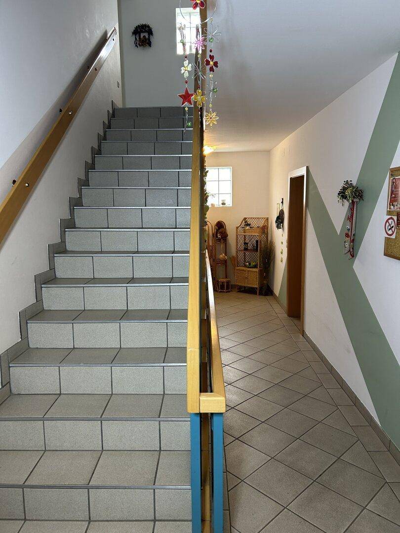 Heller Treppenaufgang mit Fliesenboden und Holzgeländer, führt zu den oberen Etagen des Hauses.