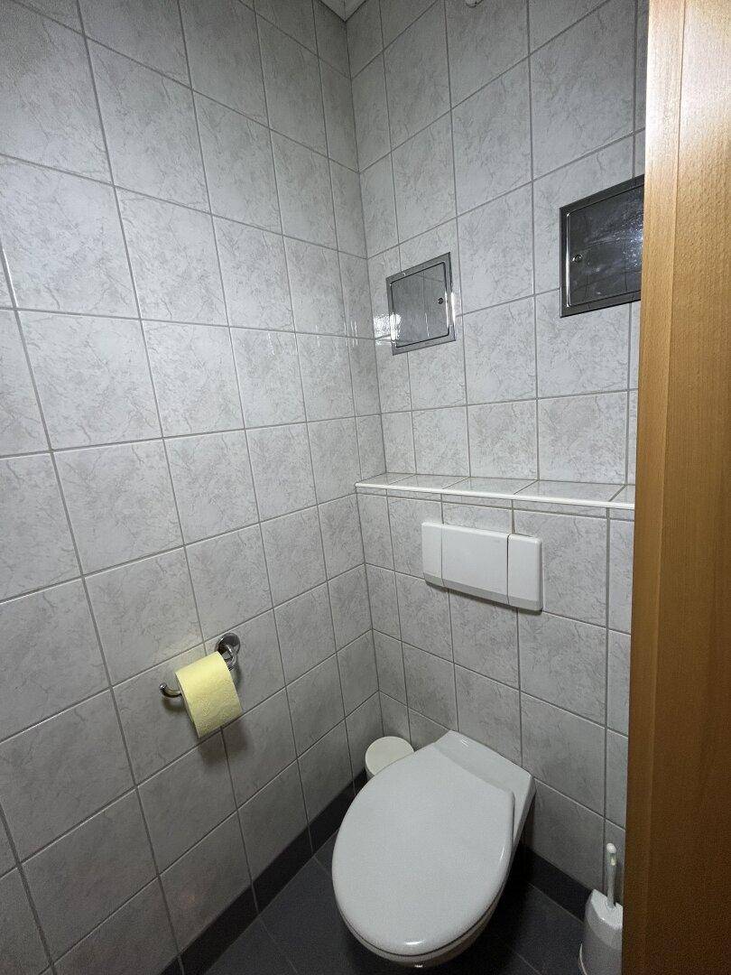 Kleines Gäste-WC mit Wand-WC und hellgrauen Fliesen an Wänden und Boden, funktional gestaltet.