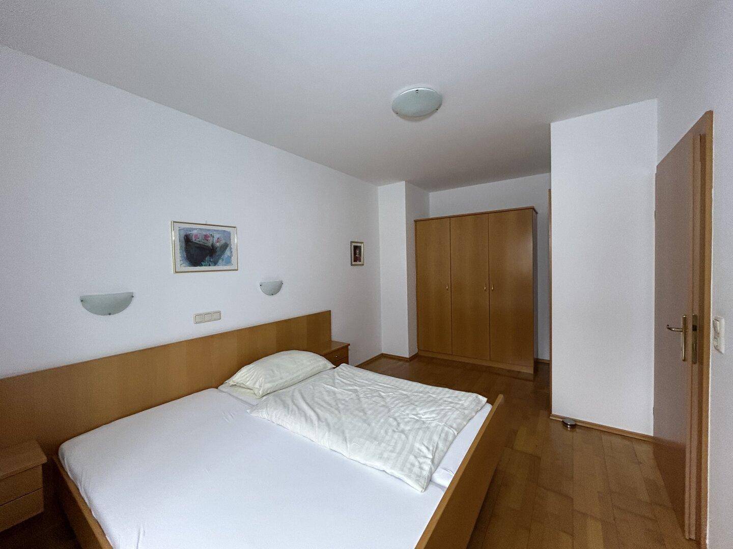 Schlafzimmer mit Doppelbett, Holzschrank und Holzboden, bietet eine ruhige Atmosphäre.