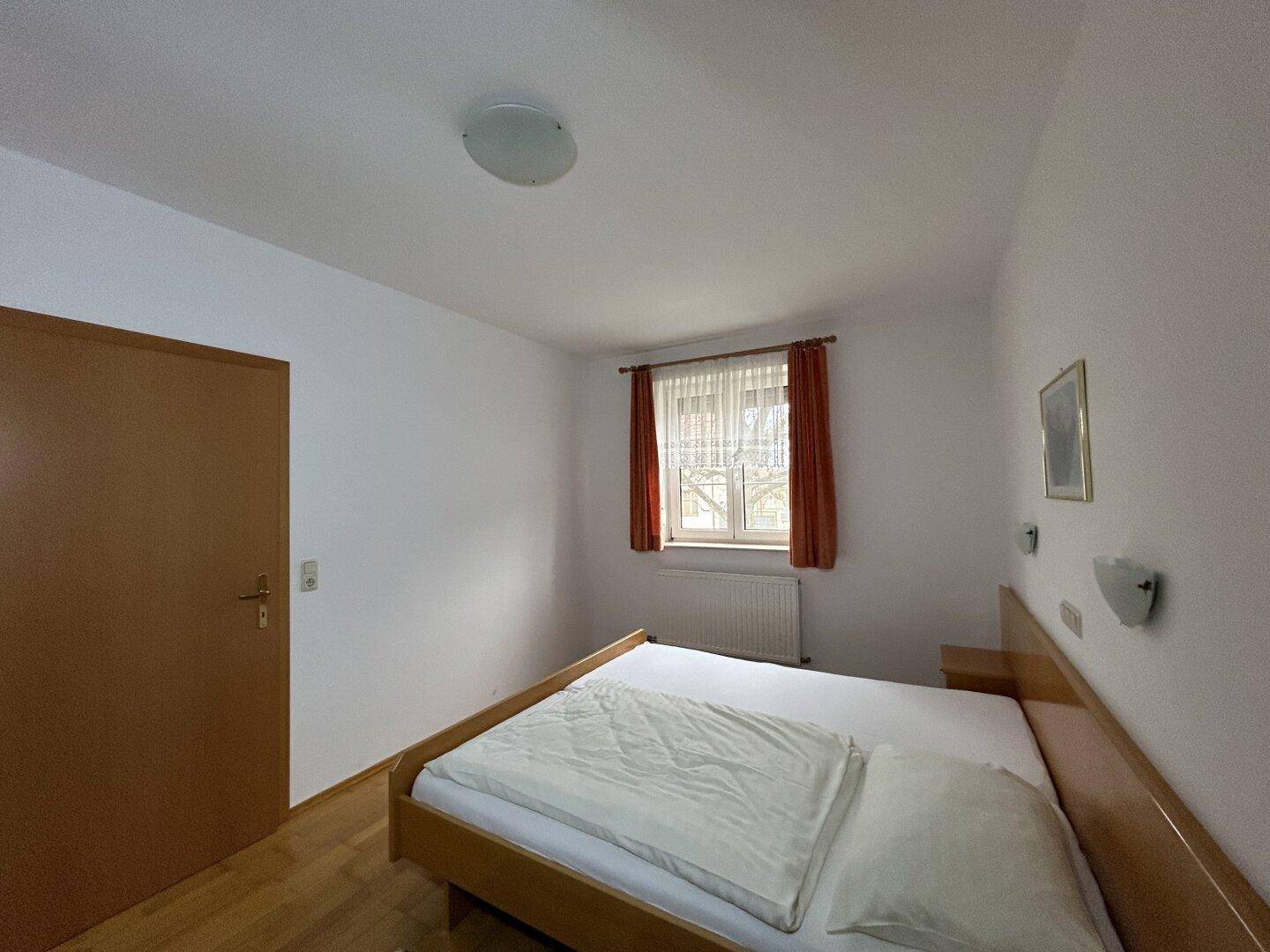 Helles Schlafzimmer mit Doppelbett, Fenster und Heizkörper, ideal für erholsamen Schlaf.