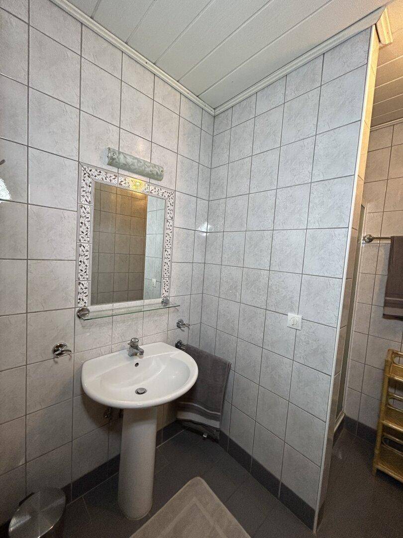 Badezimmer mit Waschbecken, Spiegel und hellgrauen Fliesen an Wänden und Boden.