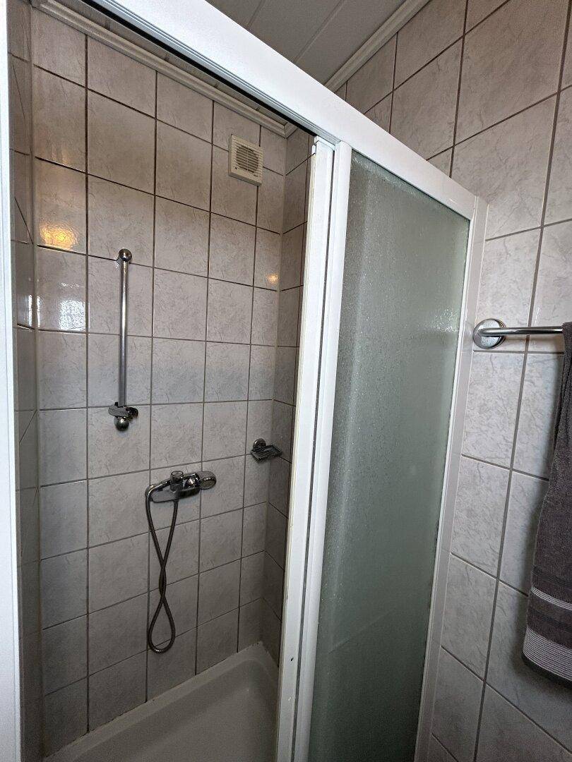 Duschbereich im Badezimmer mit Fliesenwänden und Duschkabine, funktional und sauber.