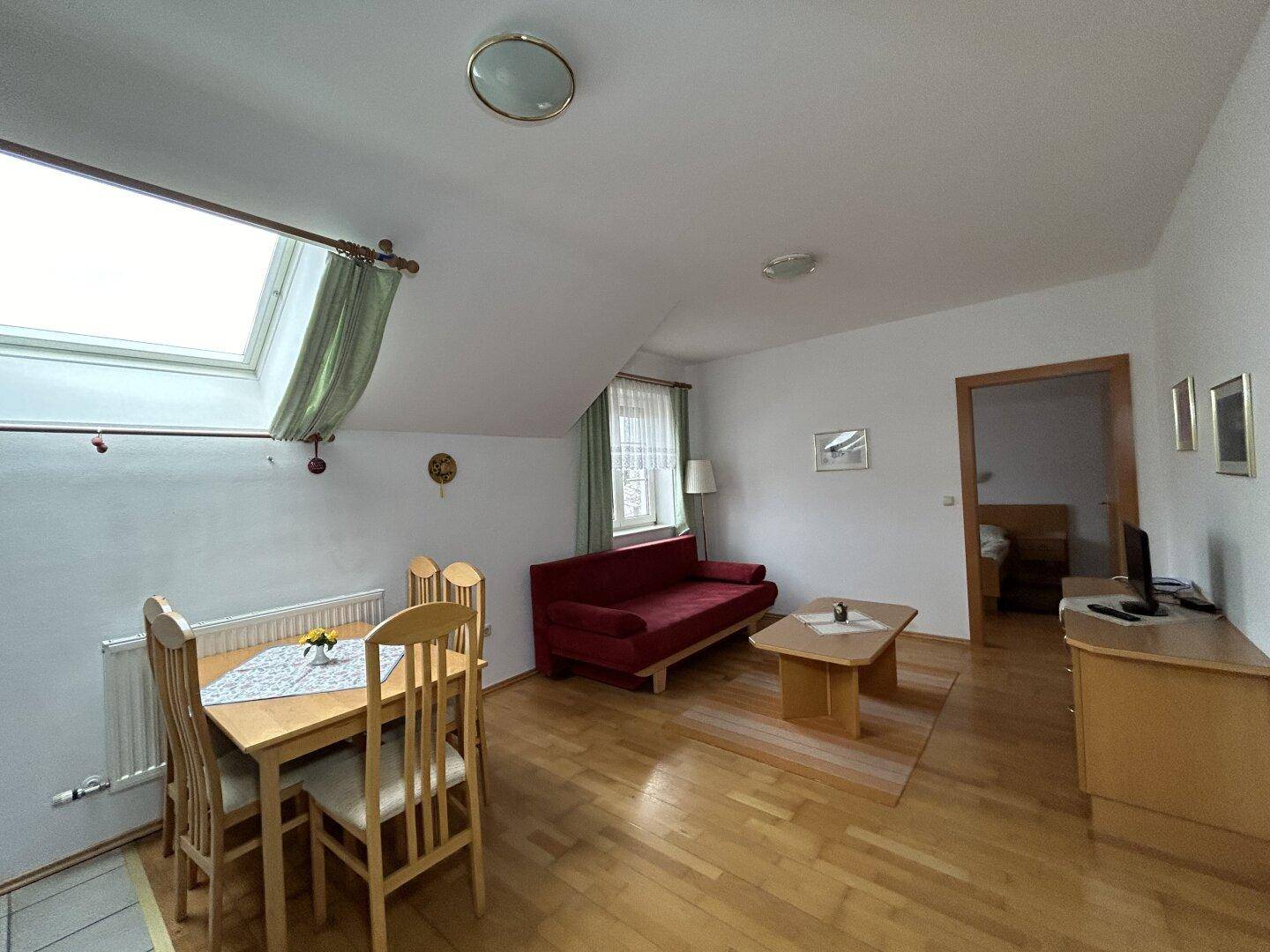 Gemütlicher Wohn- und Essbereich im Dachgeschoss mit Holzboden und Dachfenster für viel Licht.