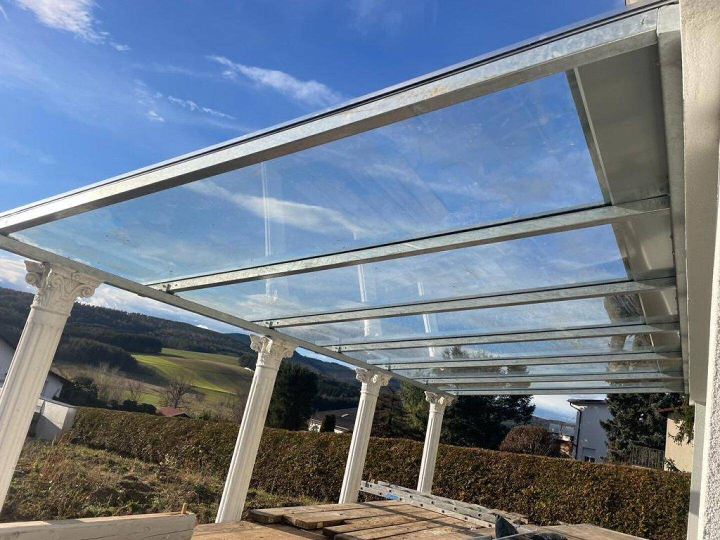 Überdachte Terrasse mit Glasdach und Säulen, bietet weiten Blick in die Landschaft.