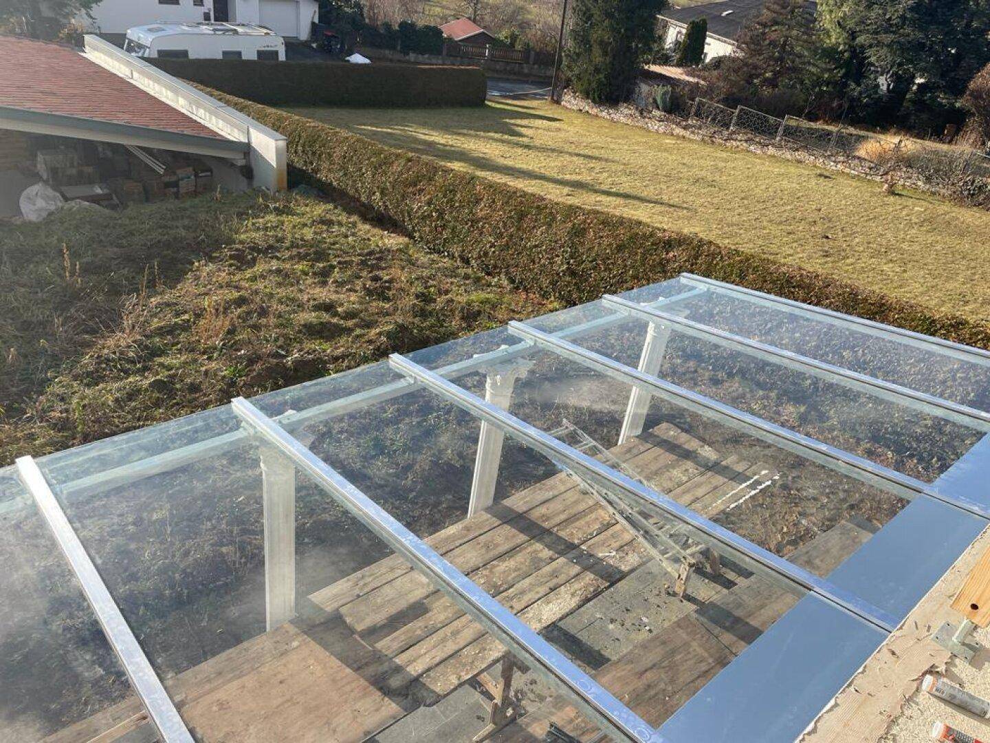 Blick von oben auf die Glasüberdachung einer Terrasse mit ländlicher Umgebung.