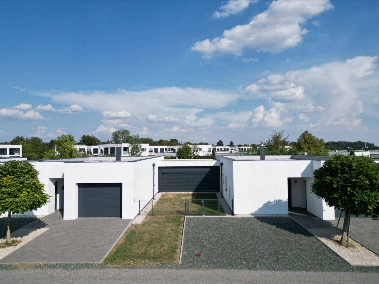 Reihen moderner Häuser mit weißer Fassade und dunklen Garagentoren, umgeben von gepflegten Außenbereichen.