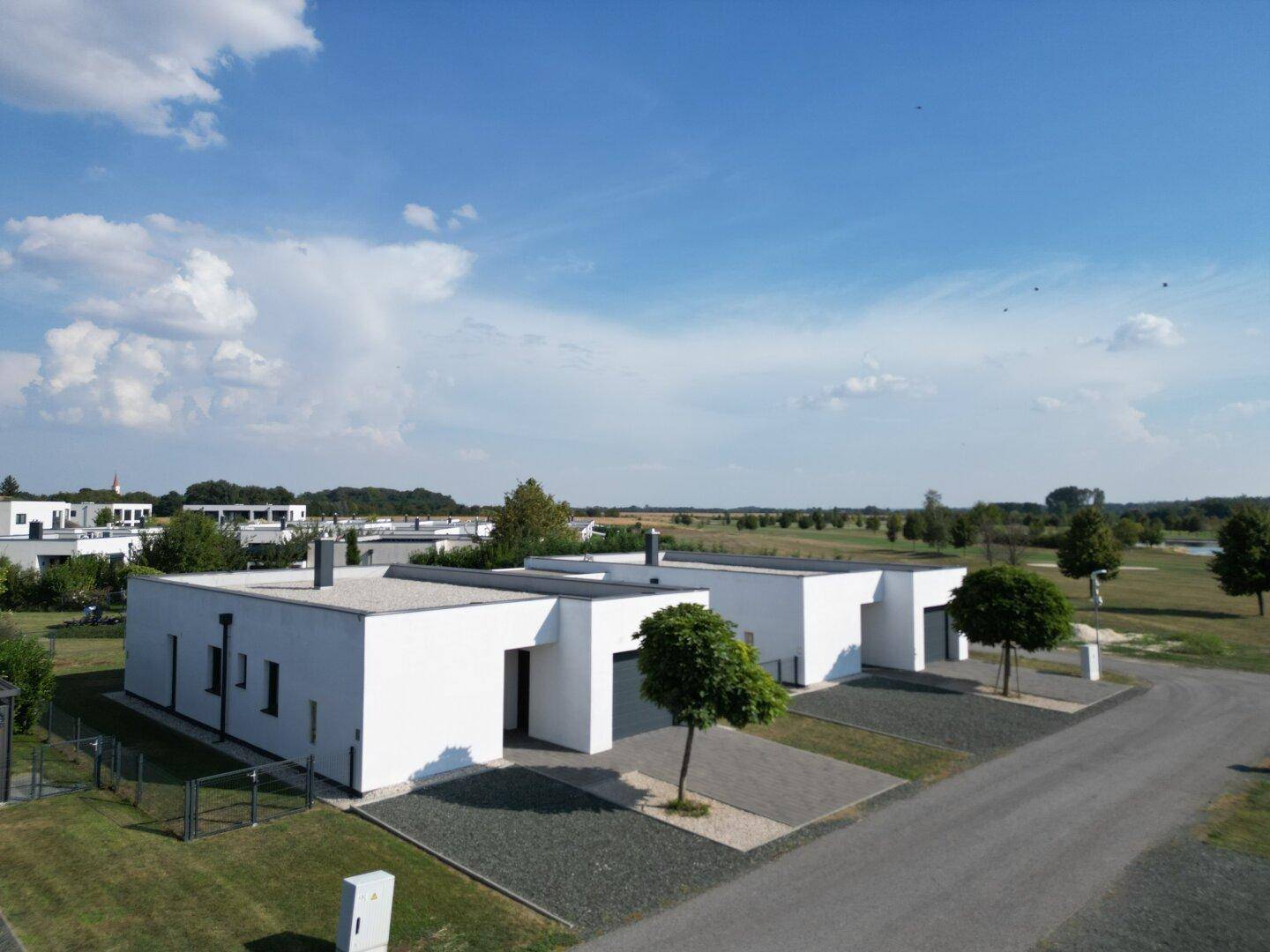 Moderne Wohnanlage mit mehreren Häusern, die sich durch klare Linien und Flachdächer in einer grünen Landschaft auszeichnen.
