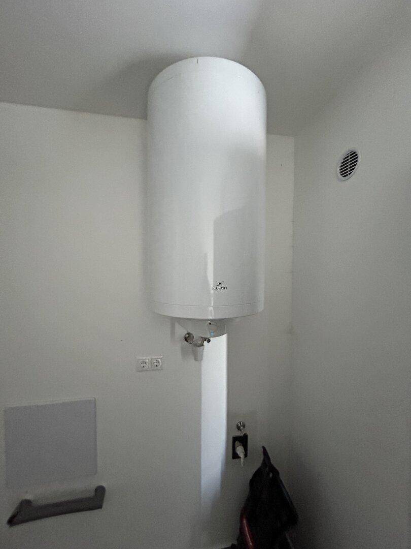 Hauswirtschaftsraum mit Warmwasserspeicher und Lüftungsgitter an der Wand.