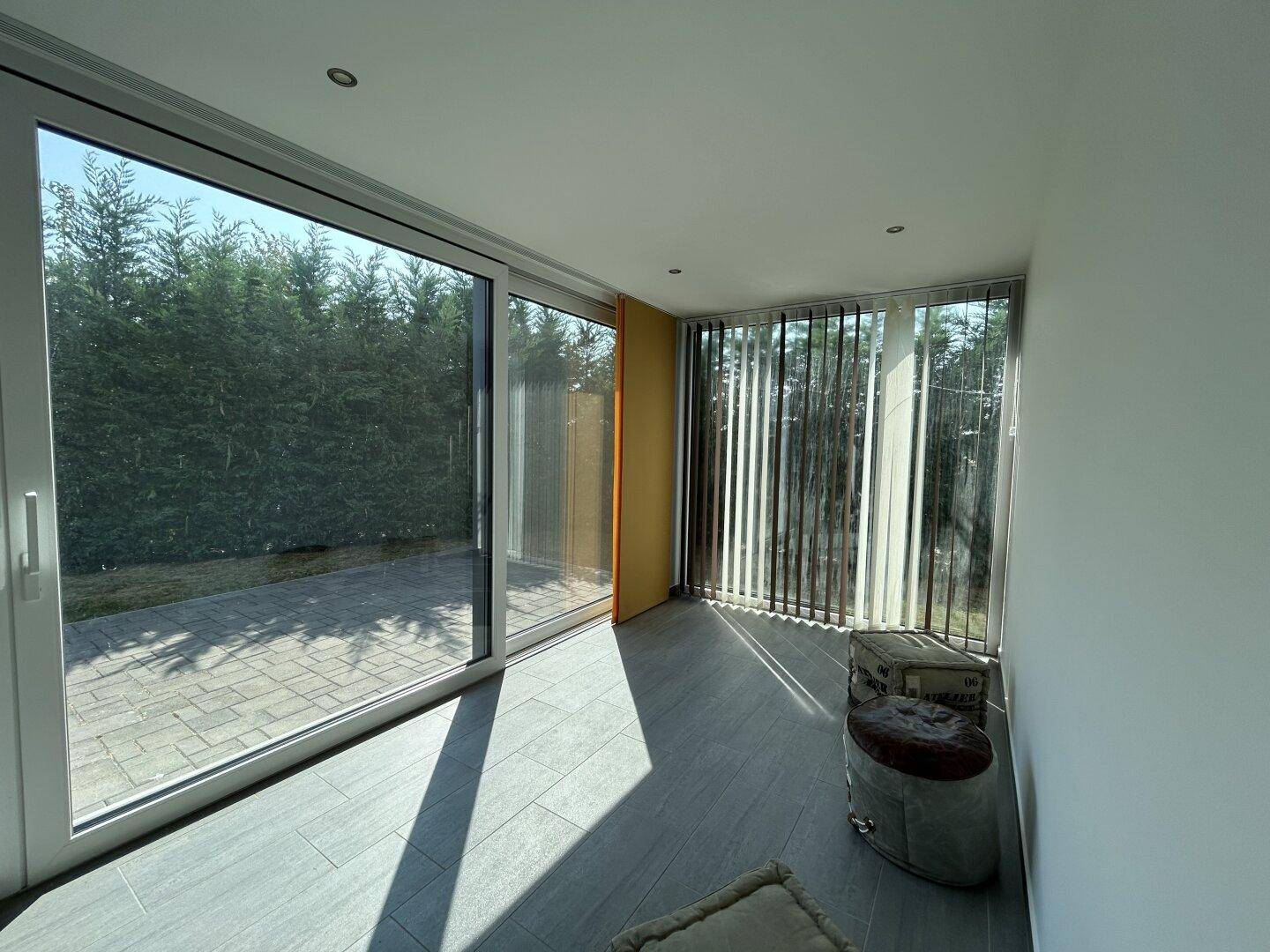 Heller Raum mit großen Glasschiebetüren zur Terrasse und vertikalen Jalousien, ideal für viel Tageslicht.