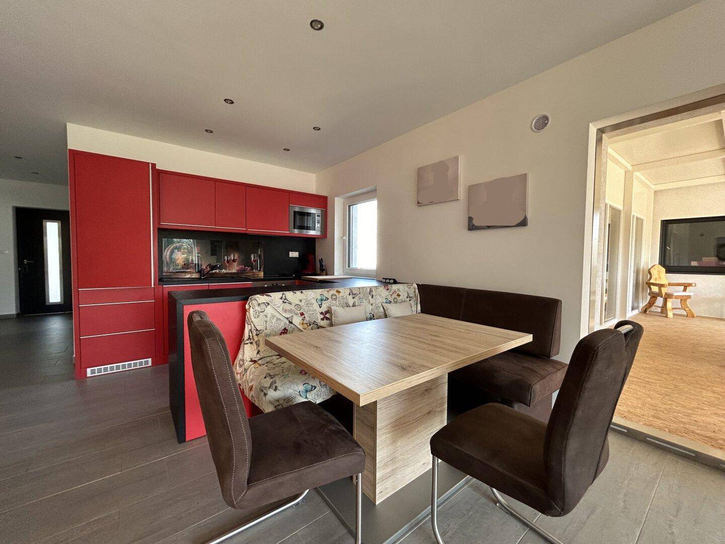 Moderne Küche mit roten Schränken und einem Essbereich mit Holztisch und gemütlicher Sitzbank.