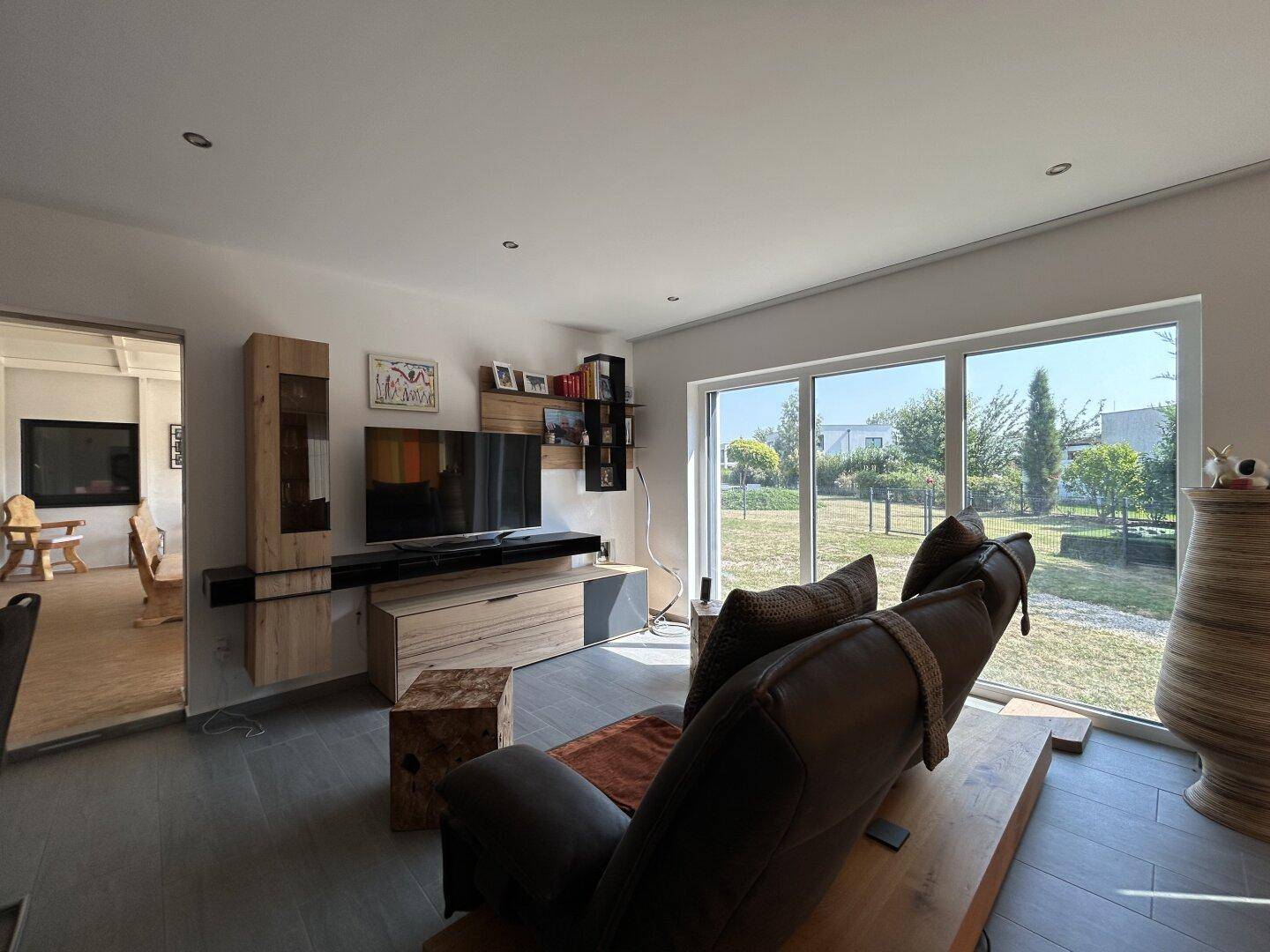 Helles Wohnzimmer mit bequemer Liege, modernem TV-Möbel und großem Fenster mit Gartenblick.