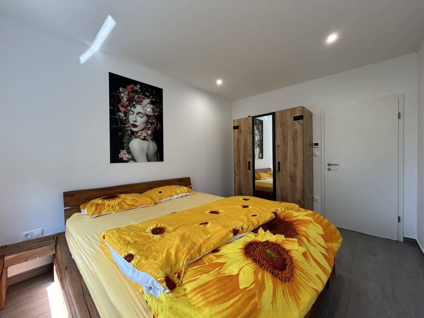 Helles Schlafzimmer mit Holzbett, Spiegelschrank und farbenfroher Bettwäsche.