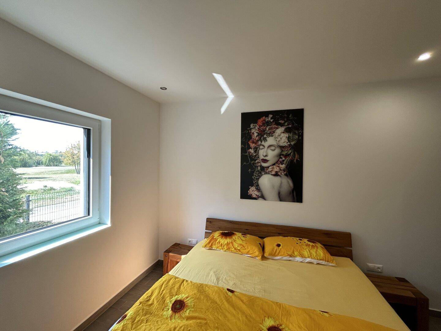 Schlafzimmer mit Fenster und Blick ins Grüne, ausgestattet mit einem Holzbett.