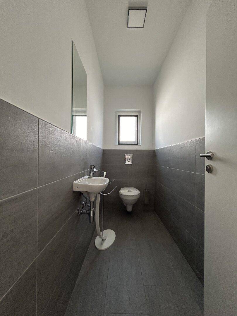 Kleines Gäste-WC mit modernem Design, Waschbecken, Toilette und einem Fenster für natürliche Belüftung.