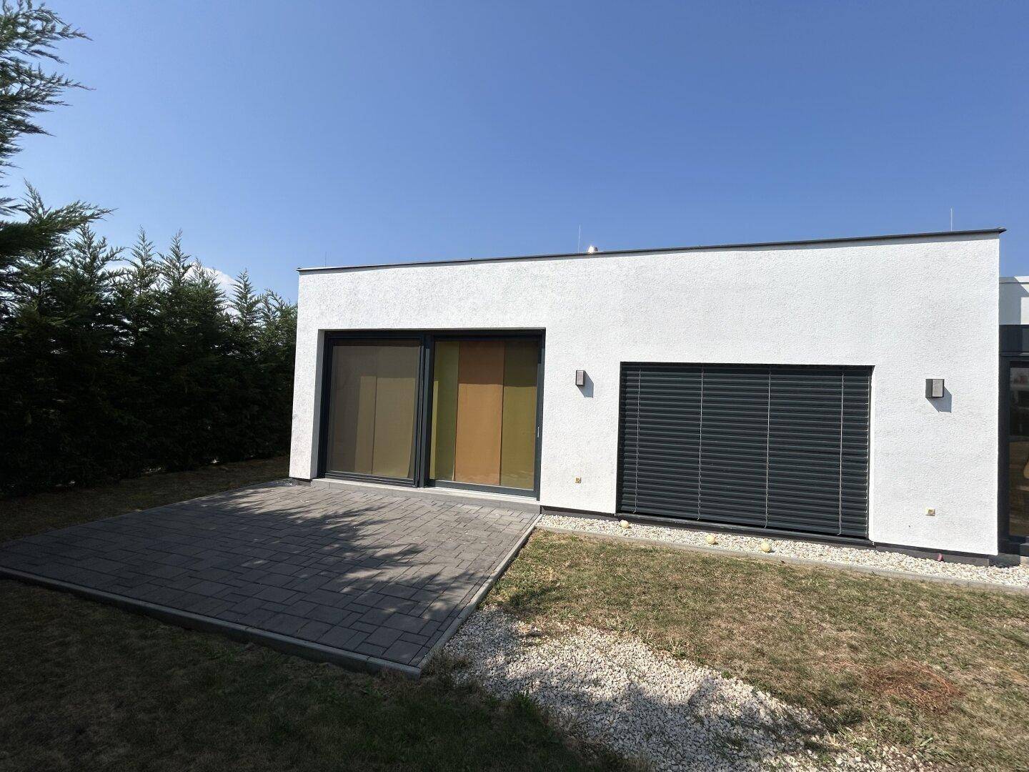 Moderne Hausfassade mit großer Schiebetür, Terrasse und angrenzendem Rasenbereich.