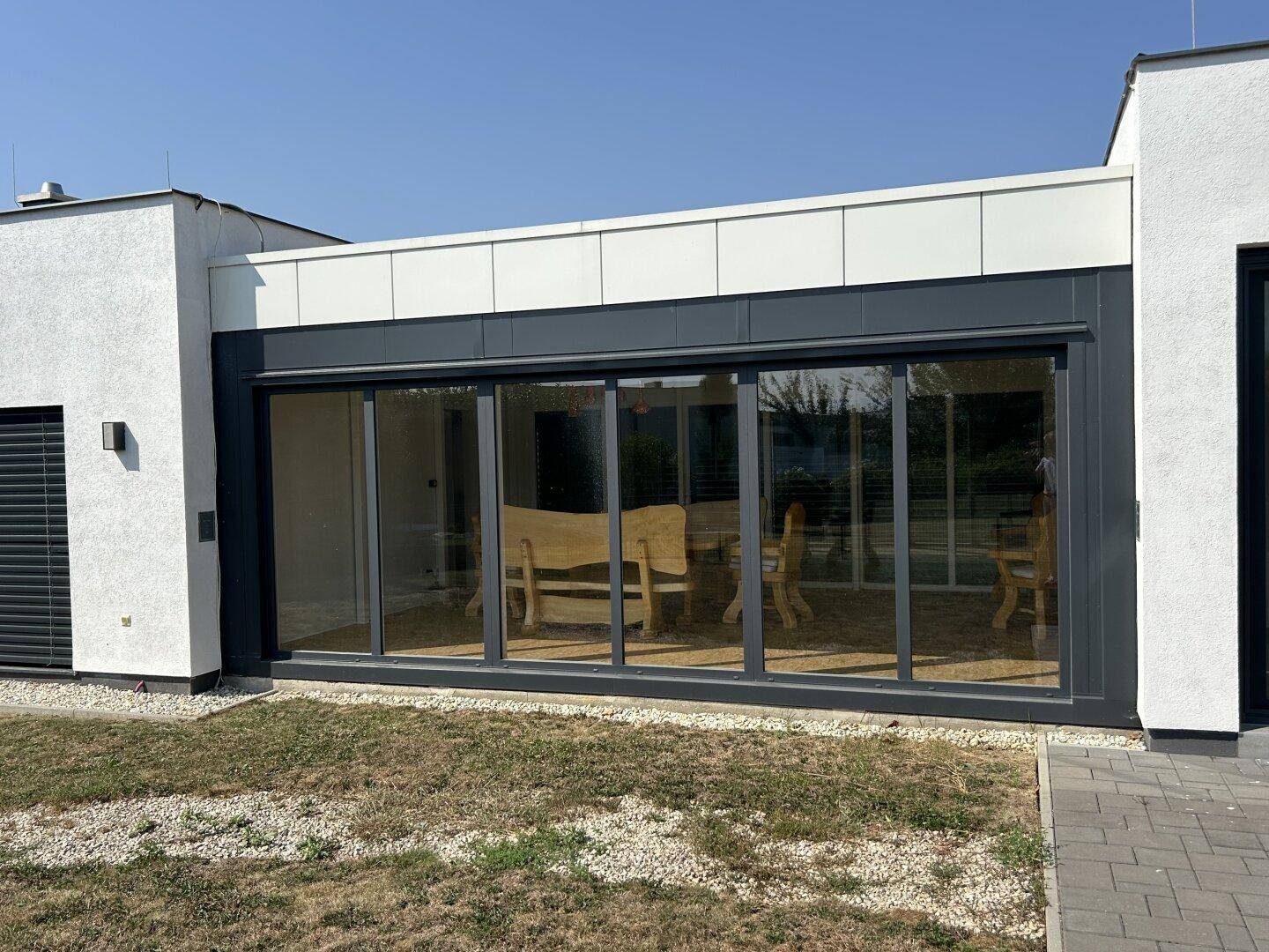 Modernes Haus mit großem verglastem Wintergarten, der rustikale Holzmöbel und viel Tageslicht bietet.