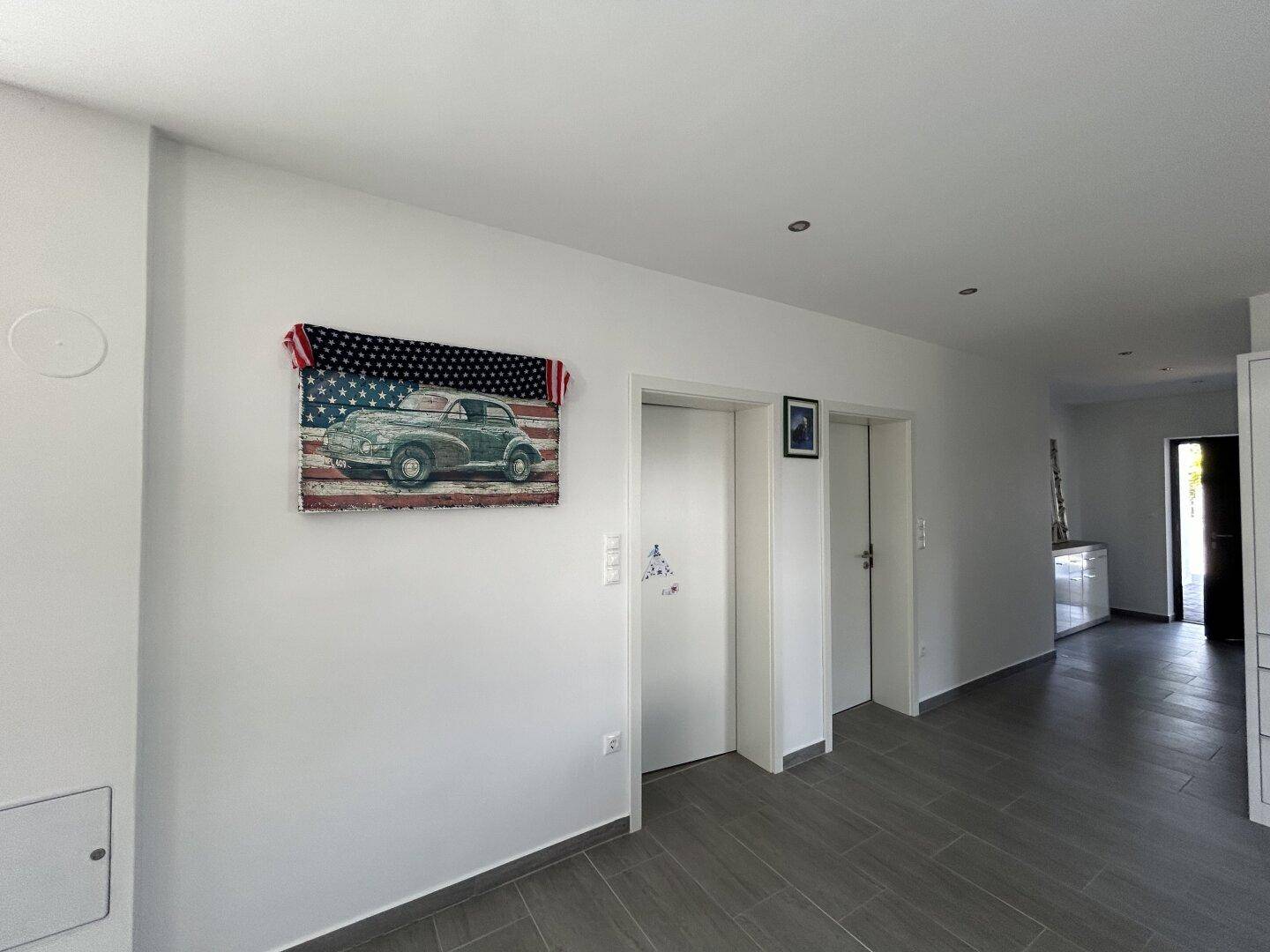 Heller Flur mit grauen Fliesen und einem dekorativen Bild, das einen Oldtimer vor amerikanischer Flagge zeigt.