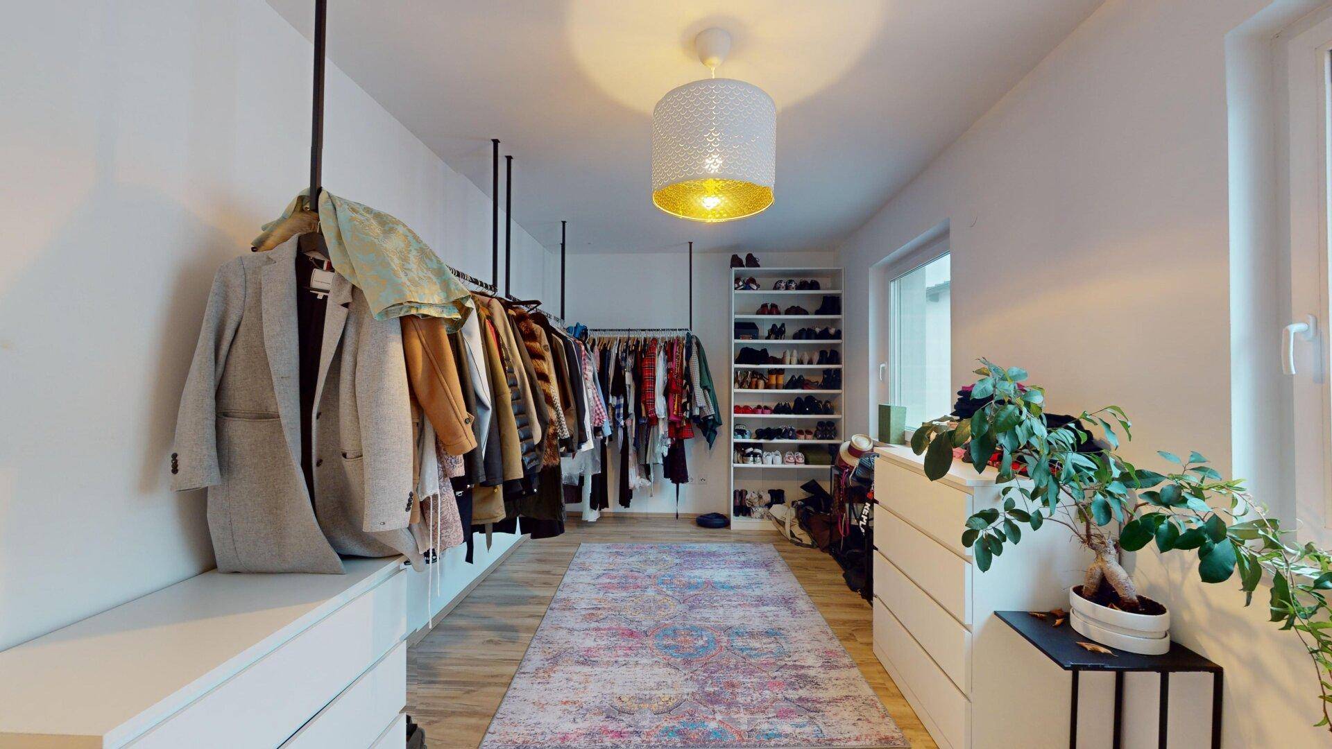 Langer begehbarer Kleiderschrank mit offener Kleiderstange und Regalen für Schuhe und Accessoires.