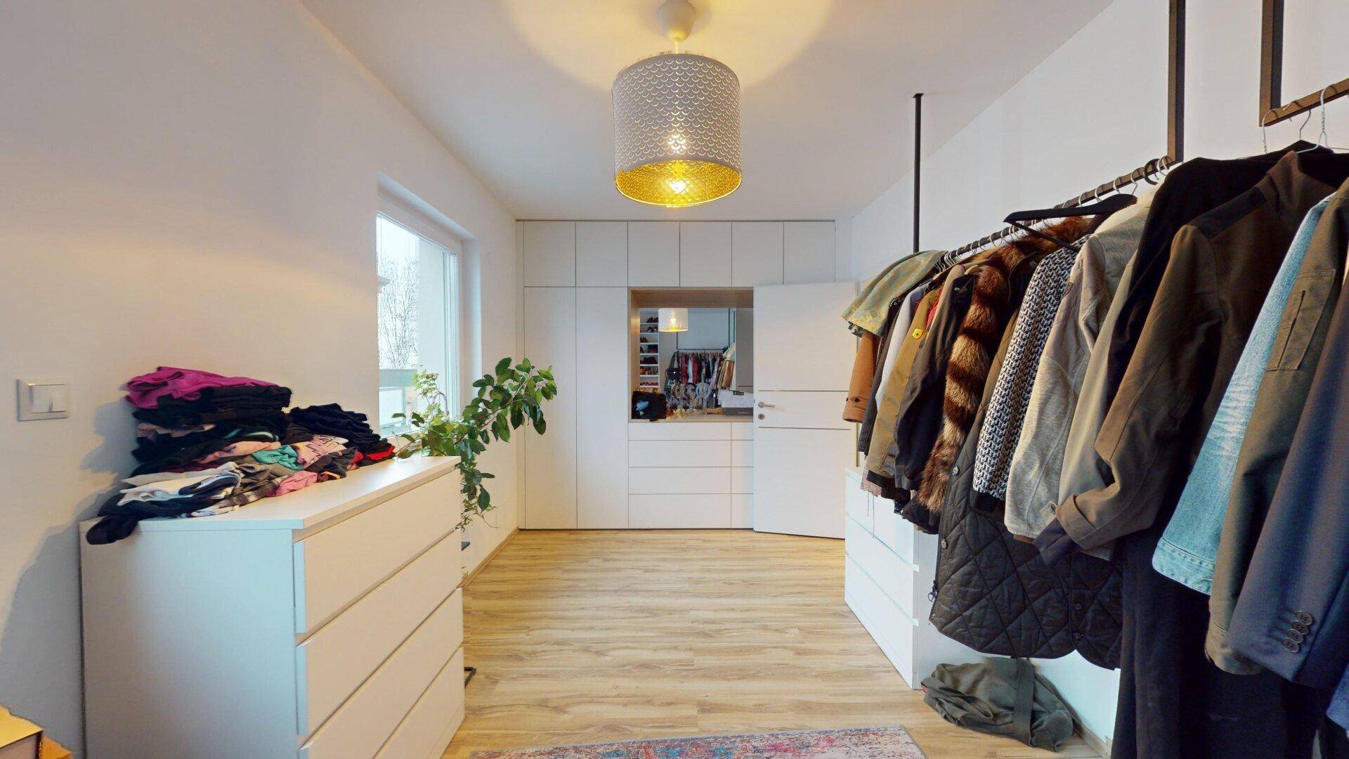 Heller begehbarer Kleiderschrank mit integriertem Spiegel und weiteren Schränken für zusätzlichen Stauraum.