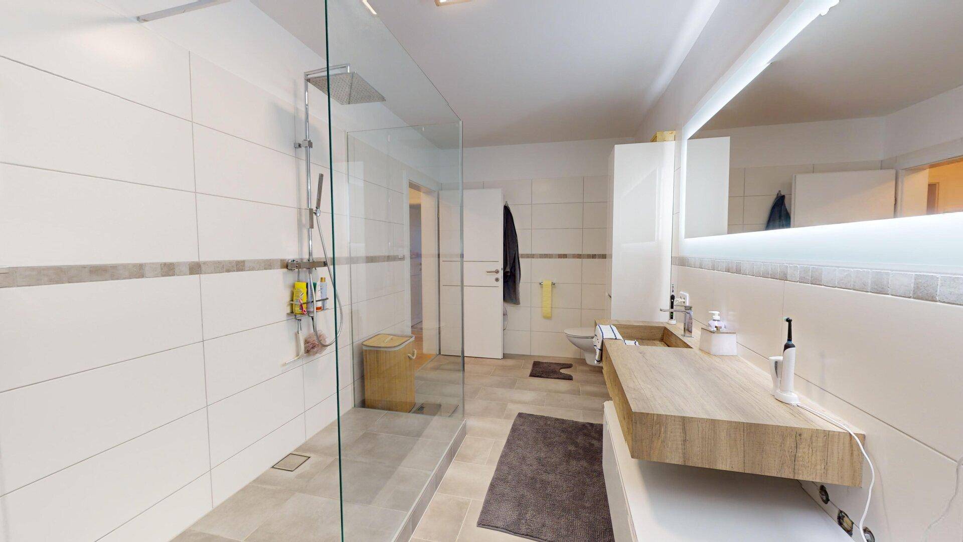 Modernes Badezimmer mit großer begehbarer Dusche, Doppelwaschbecken und hellen Fliesen.