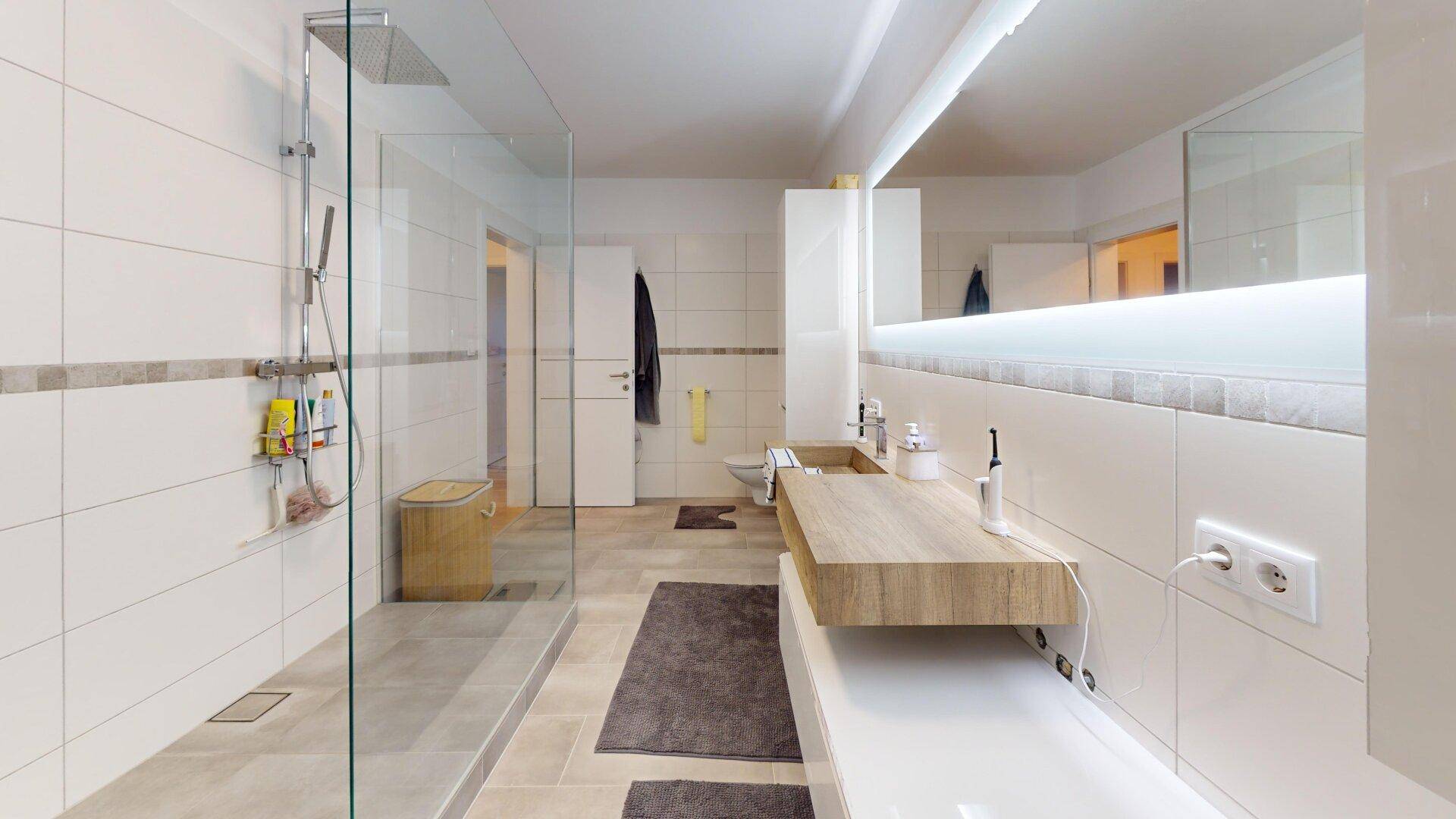Modernes Badezimmer mit großer begehbarer Dusche und Doppelwaschbecken in hellen Farbtönen.