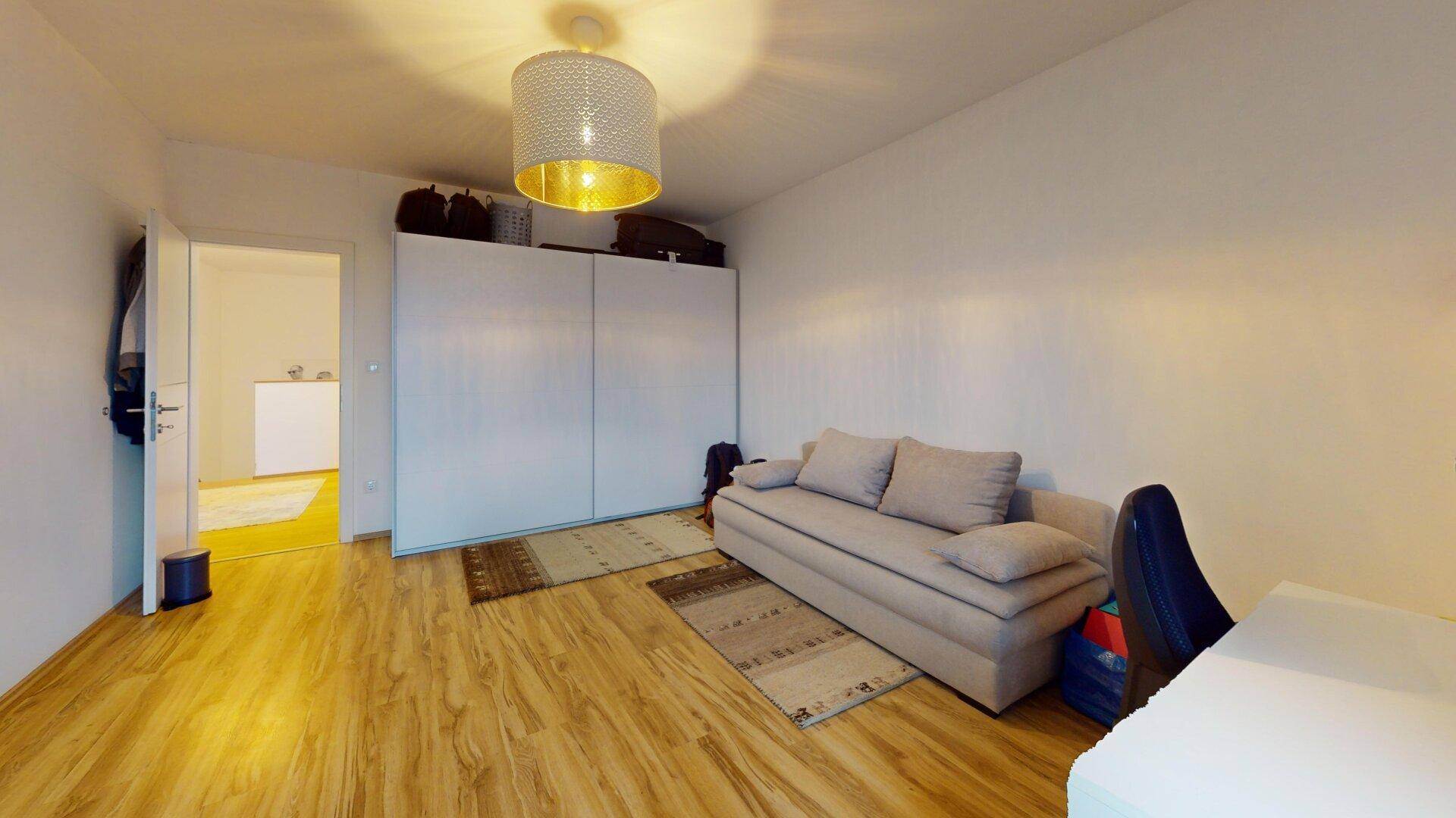 Gemütliches Wohnzimmer mit Sofa, großem Kleiderschrank und hellem Laminatboden.