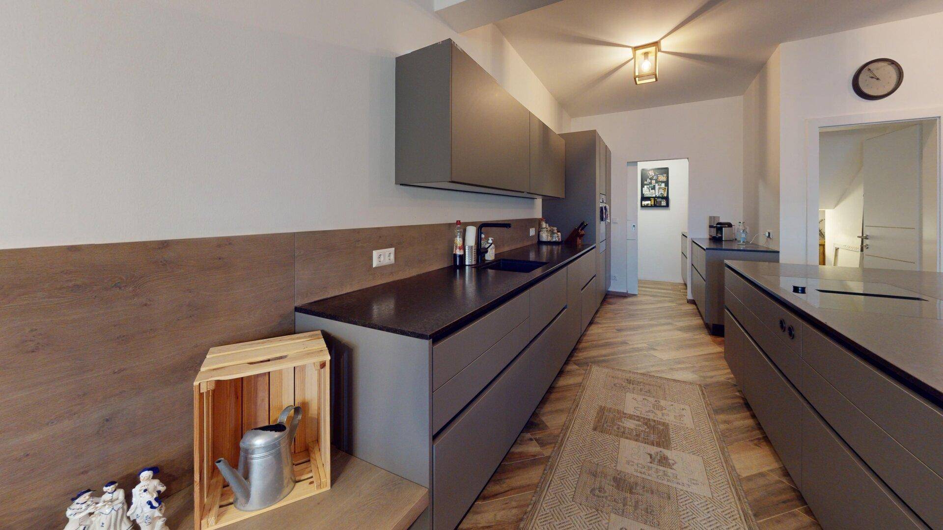 Moderne Küche mit grauen Schränken, dunklen Arbeitsplatten und Holzoptik-Boden.