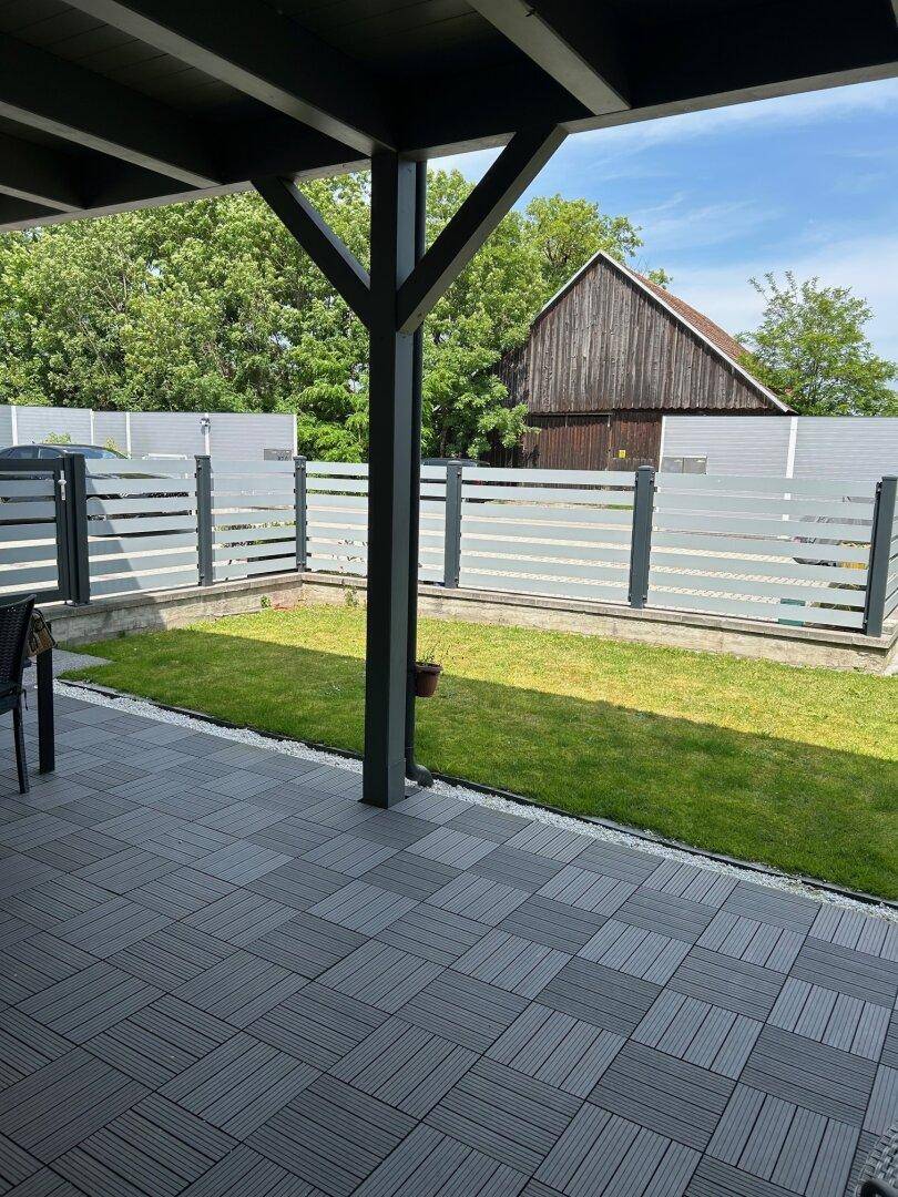 Überdachte Terrasse mit modernem Fliesenboden und kleinem, gepflegtem Rasenbereich.