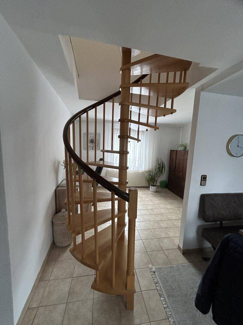 Helle Diele mit einer eleganten Holzwendeltreppe und Fliesenboden.