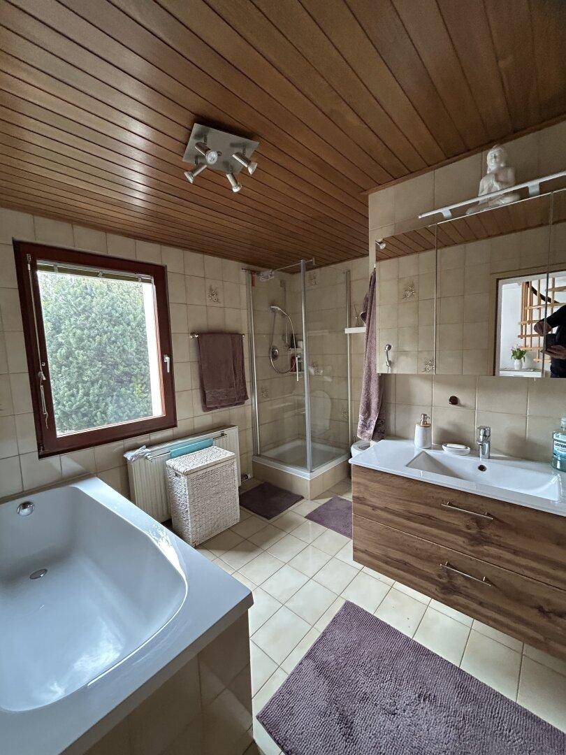 Badezimmer mit Holzdecke, Badewanne, Dusche und Fenster.