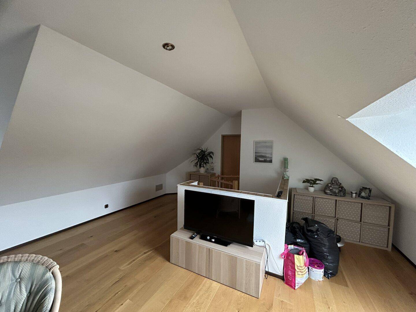 Dachgeschoss-Wohnbereich mit Holzboden, Fernseher und Stauraum unter der Schräge.