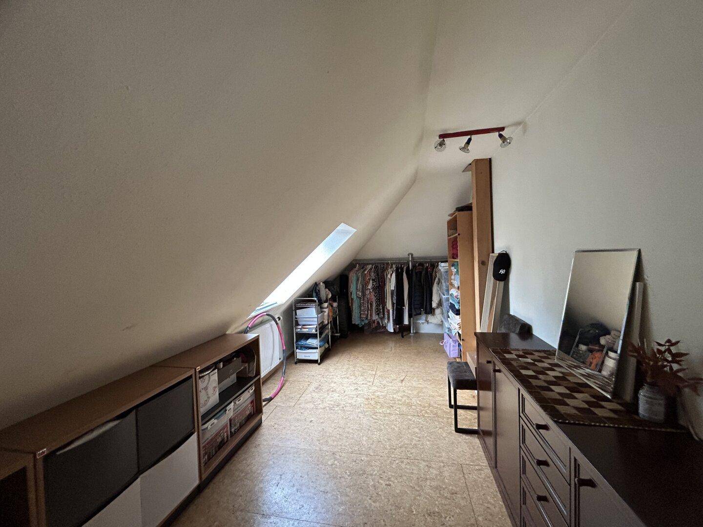 Dachgeschossraum mit Stauraum, Kleiderstangen und Dachfenster.