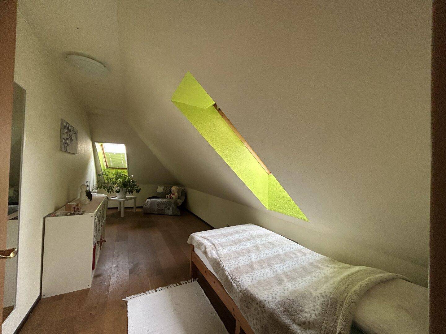 Helles Schlafzimmer im Dachgeschoss mit Einzelbett, Holzboden und Dachfenster.